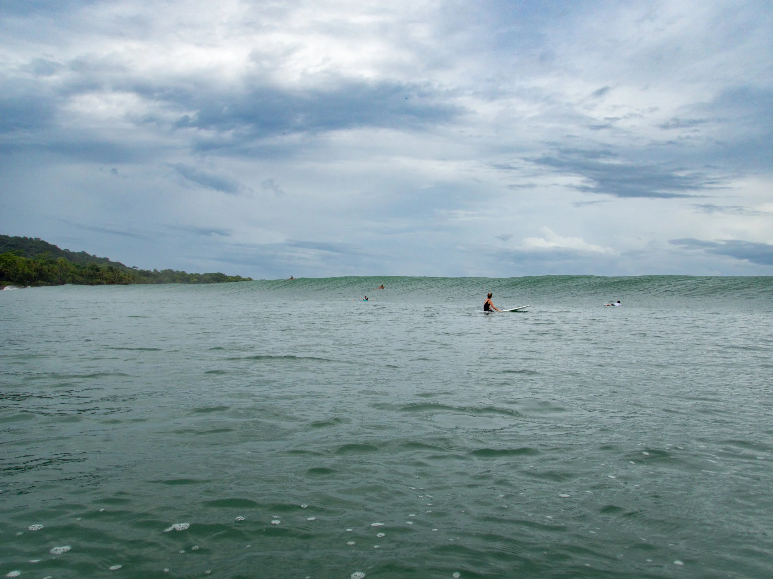 Surfers sitting on surfboards in the ocean with waves and cloudy sky