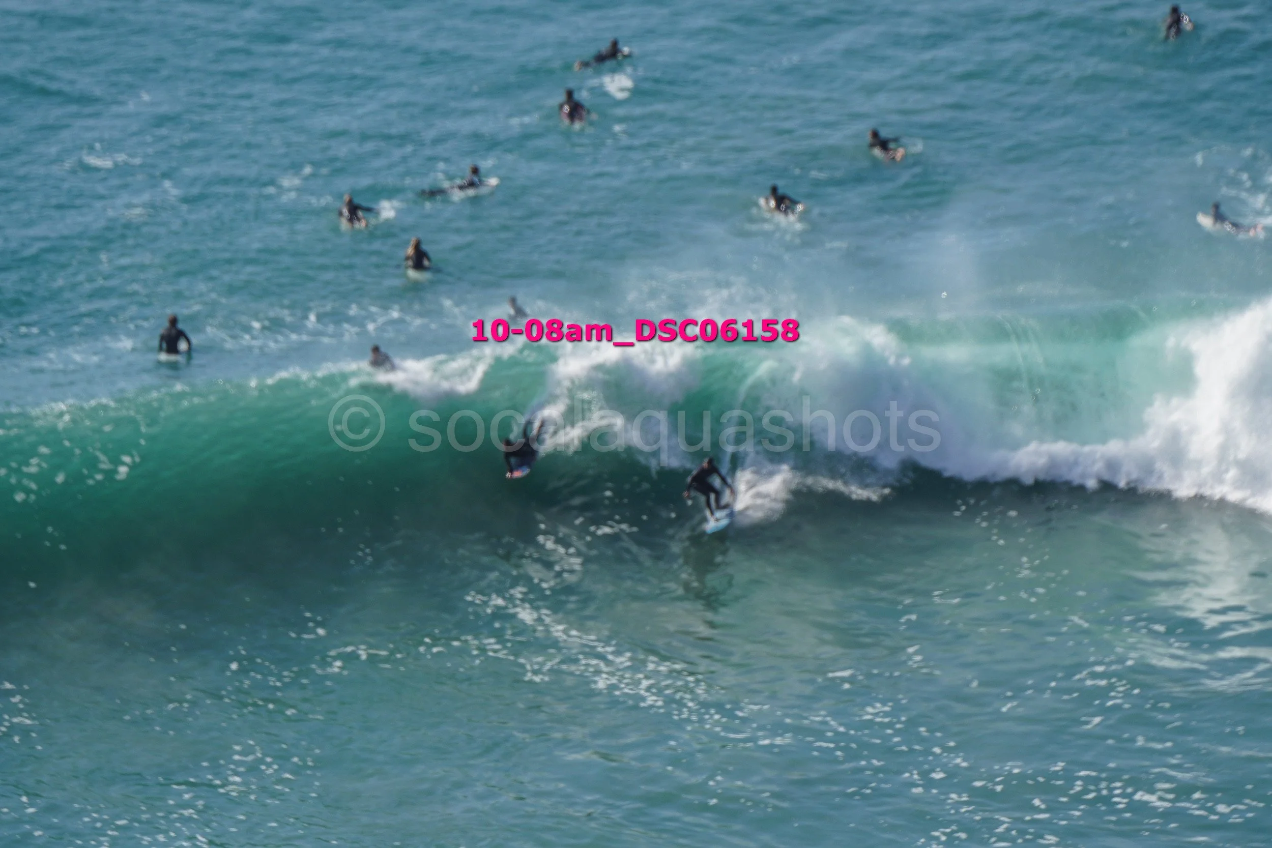 Multiple surfers riding and waiting on large ocean waves during daytime beach surfing session.