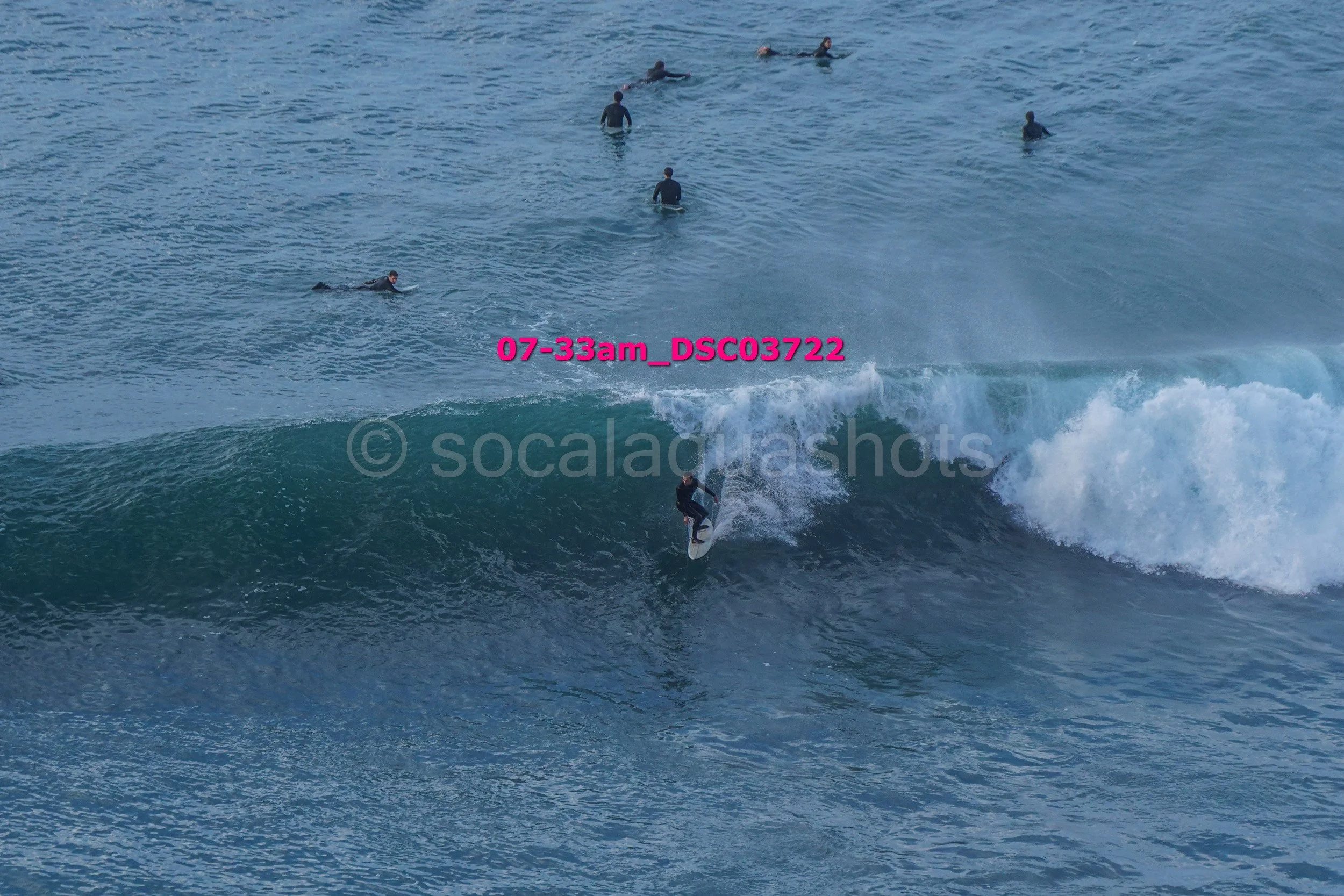A surfer riding a wave with several people swimming in the ocean in the background.