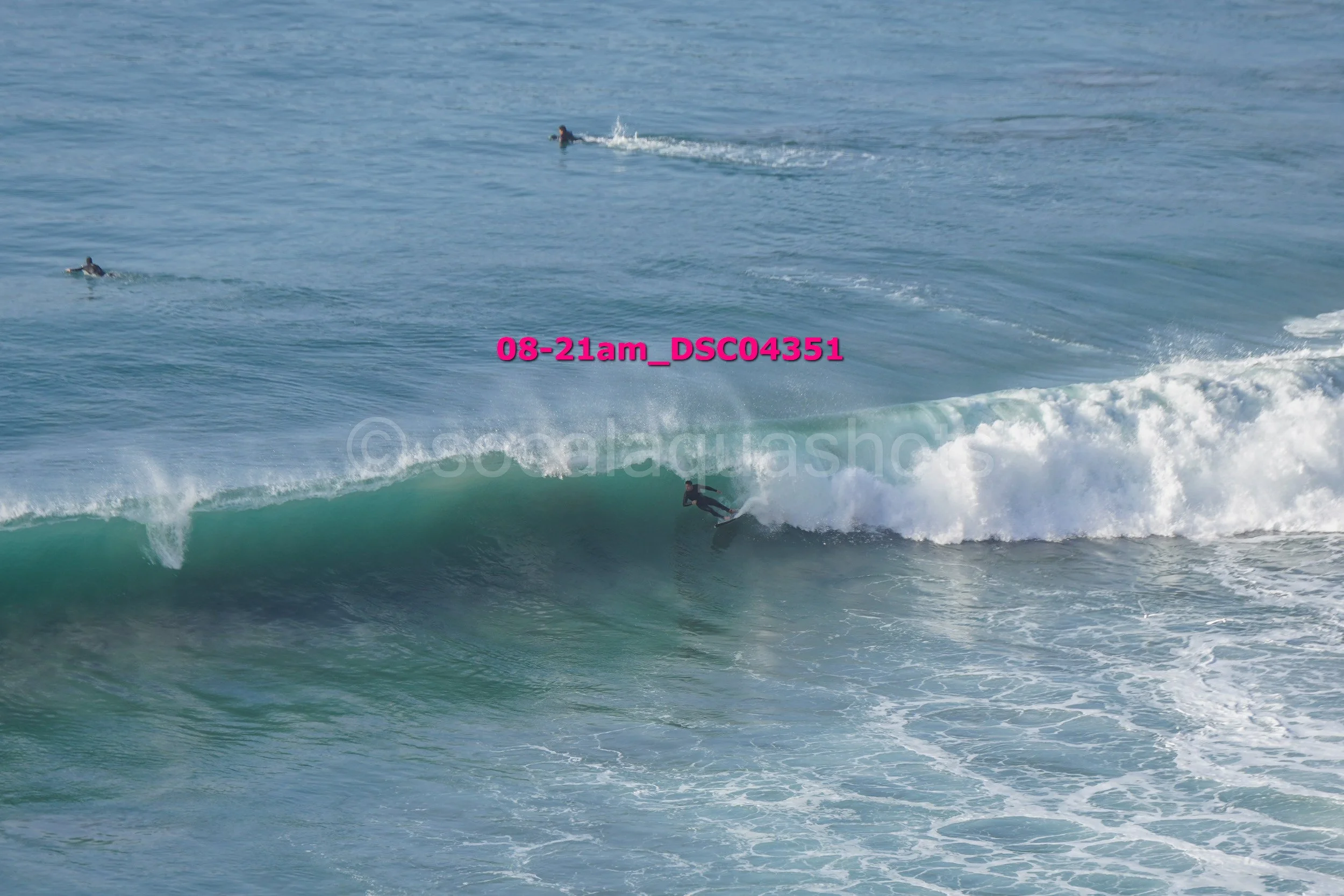 Surfer riding a wave in the ocean with two other surfers in the water in the background.