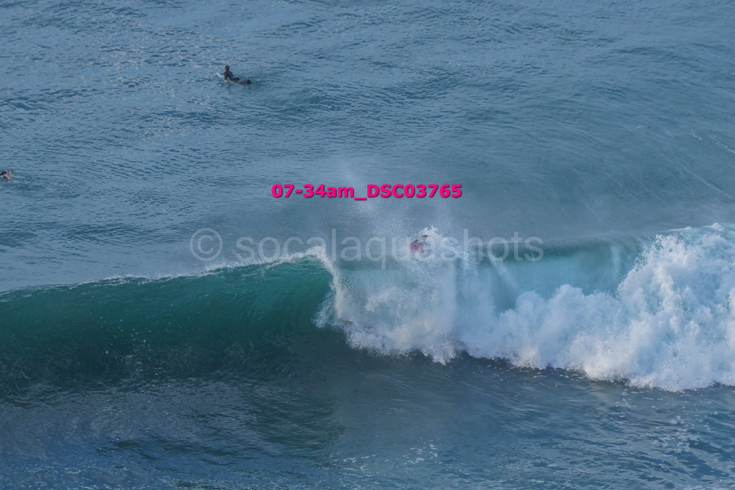 Surfer riding a wave in the ocean, with other surfers in the water nearby.