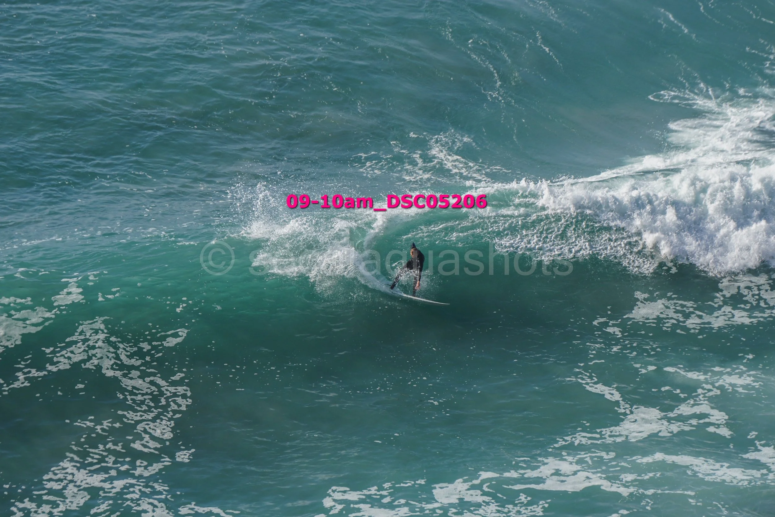 A person surfing on a large wave in the ocean with a timestamp overlay of '09-10am_DSC5206'.