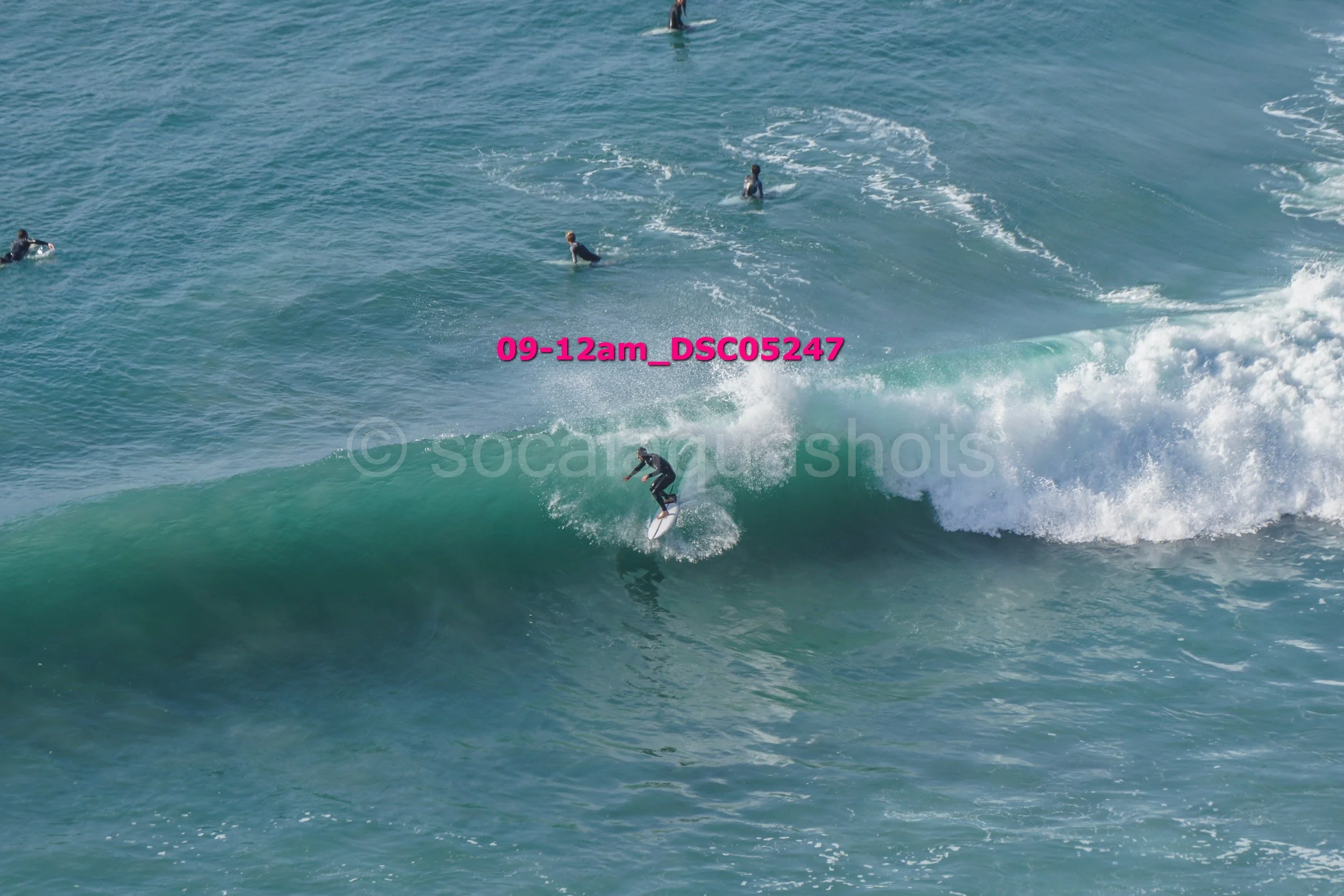 A person surfing on a wave in the ocean with several other surfers in the background.