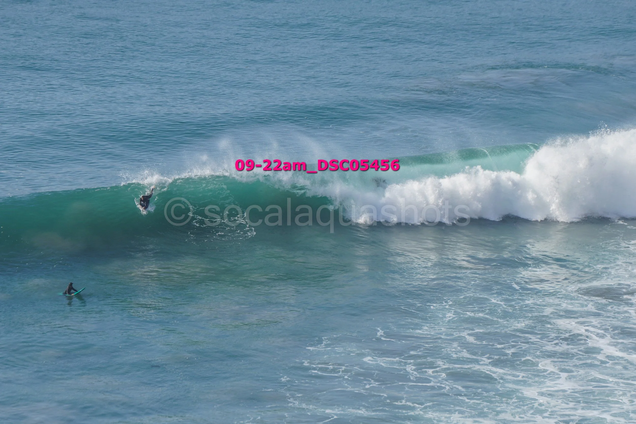 A surfer riding a large wave in the ocean, with another surfer on a surfboard in the water nearby.