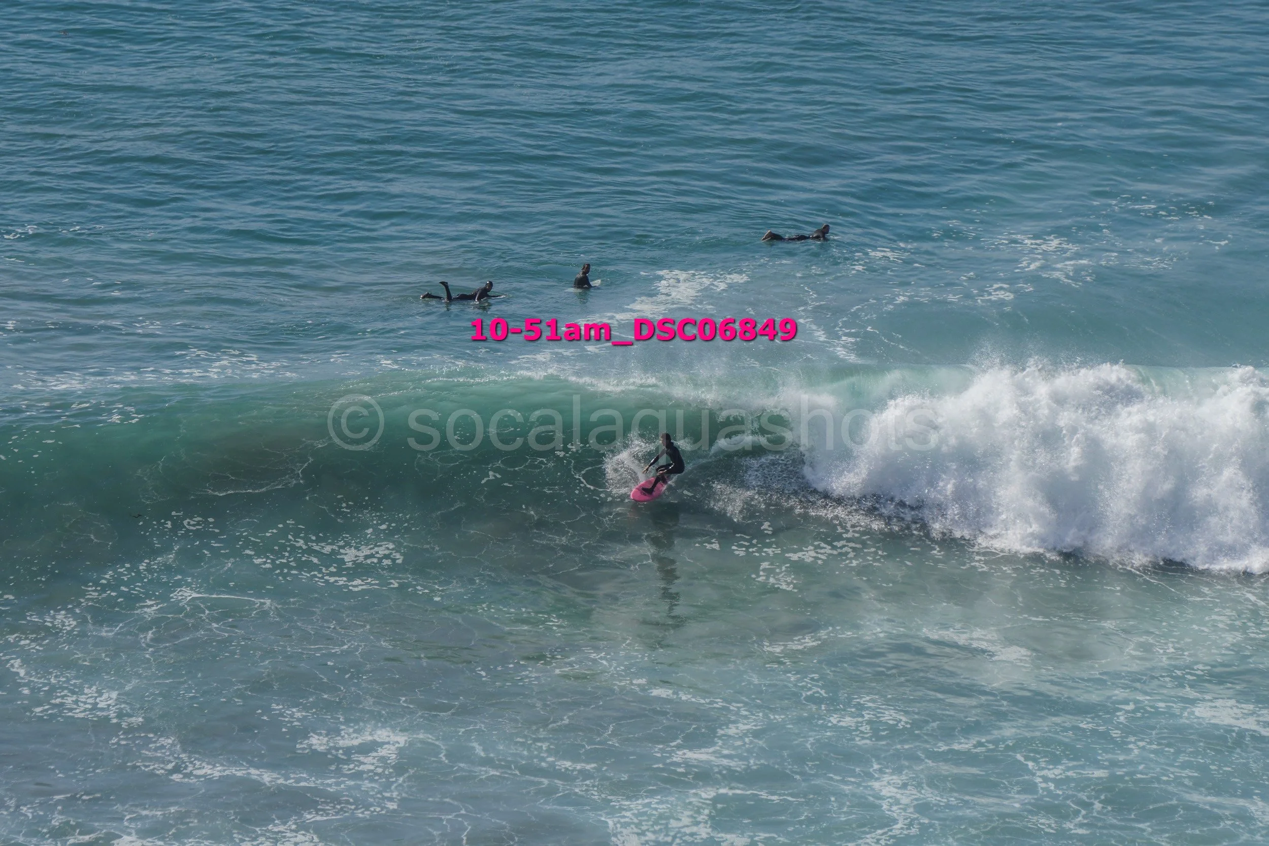 A surfer riding a wave while four paddleboarders watch in the background on the ocean.