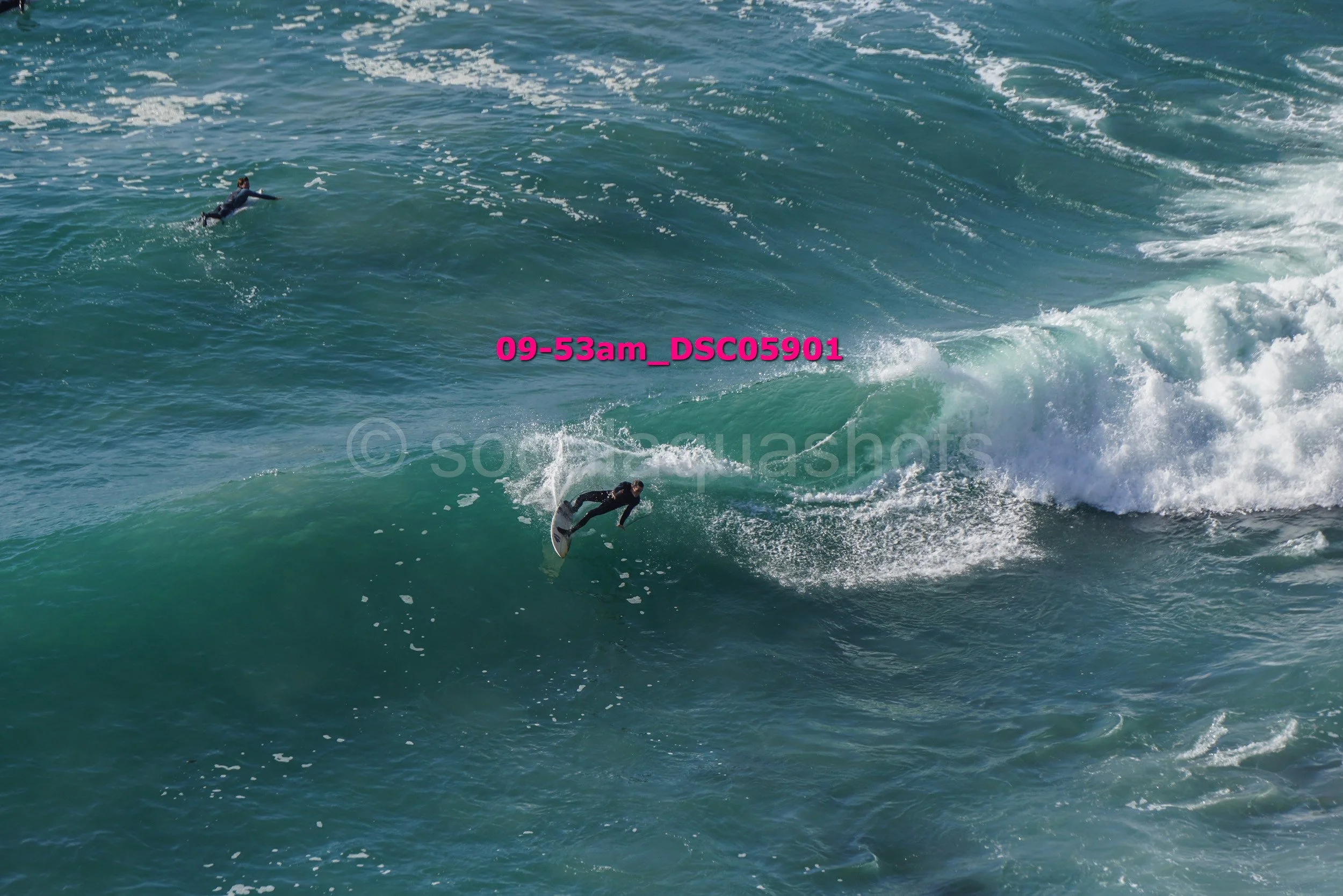 Two surfers riding and paddling on large ocean waves with white foam.