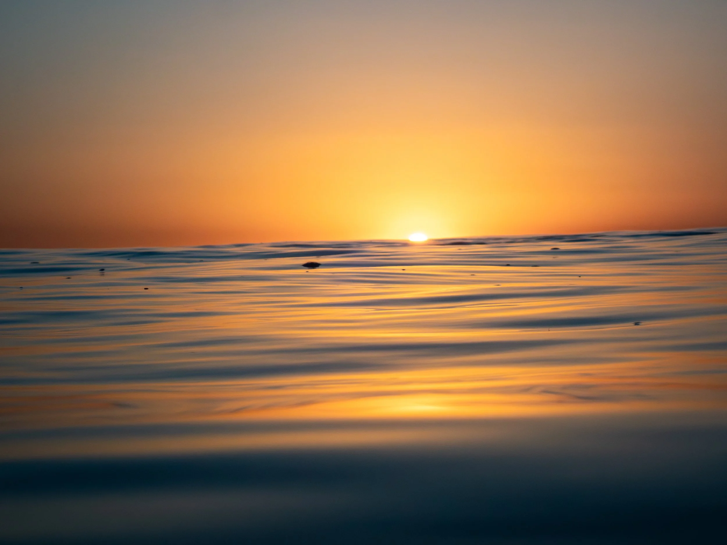 Sunset over calm ocean with orange and yellow sky reflected on water.