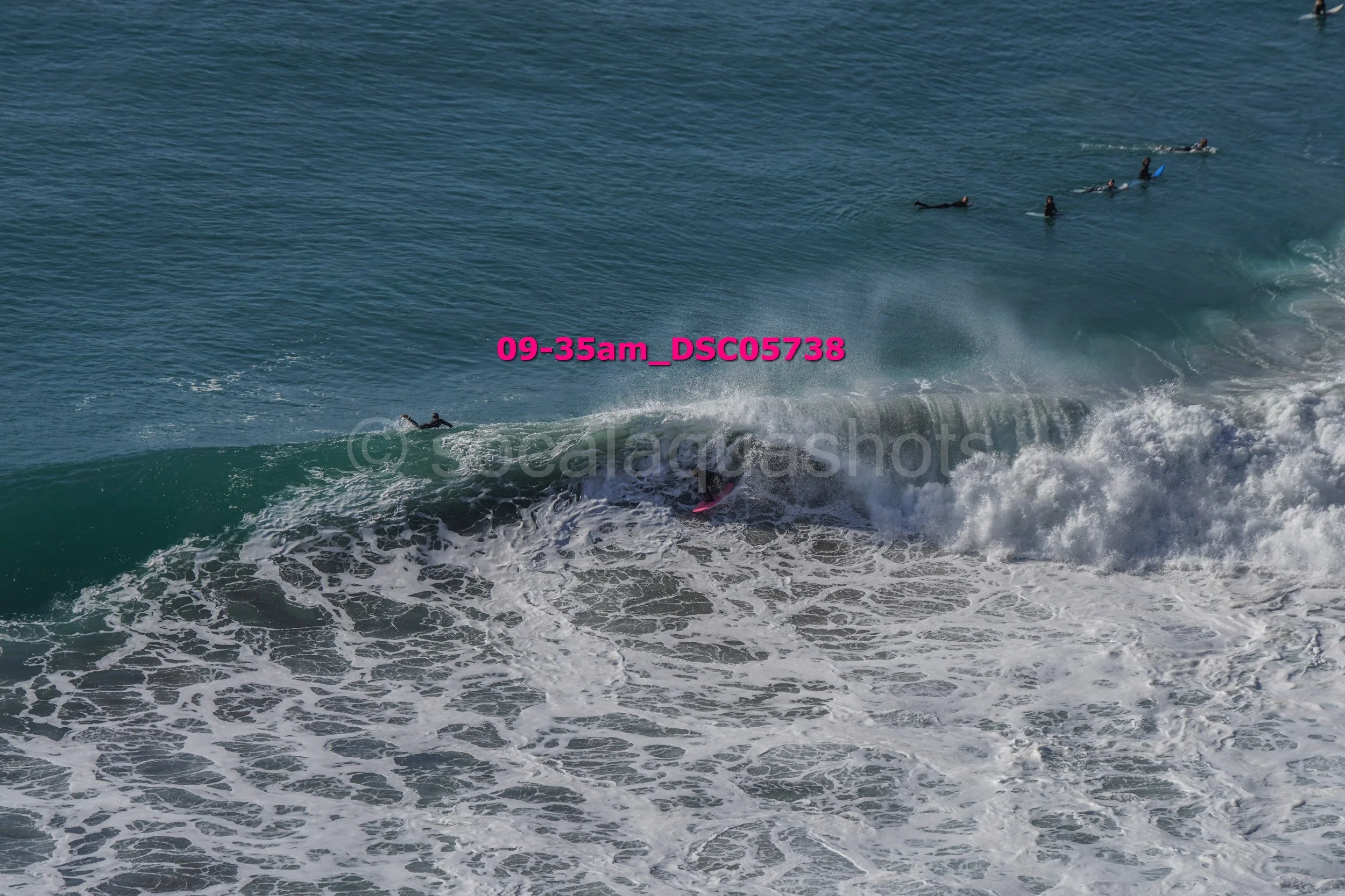 Surfer riding a wave at the beach, with several other surfers in the water in the background.