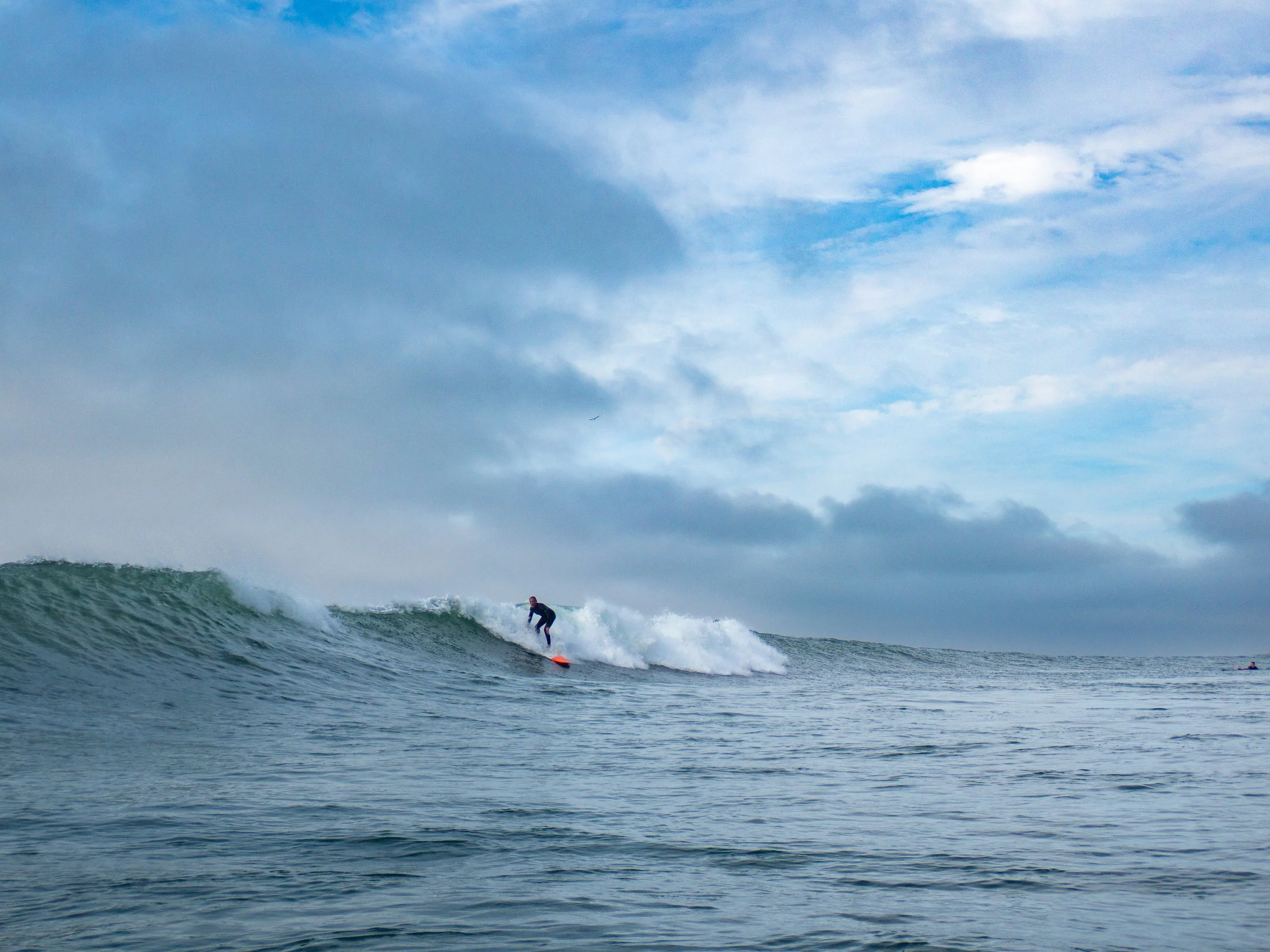 A person surfing on a wave in the ocean with a cloudy sky above.