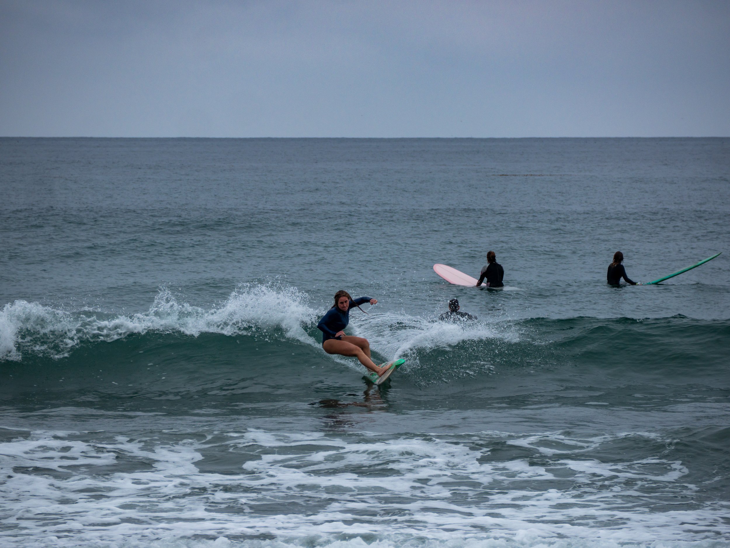 Young woman surfing on a wave at the beach with three other surfers in the background.