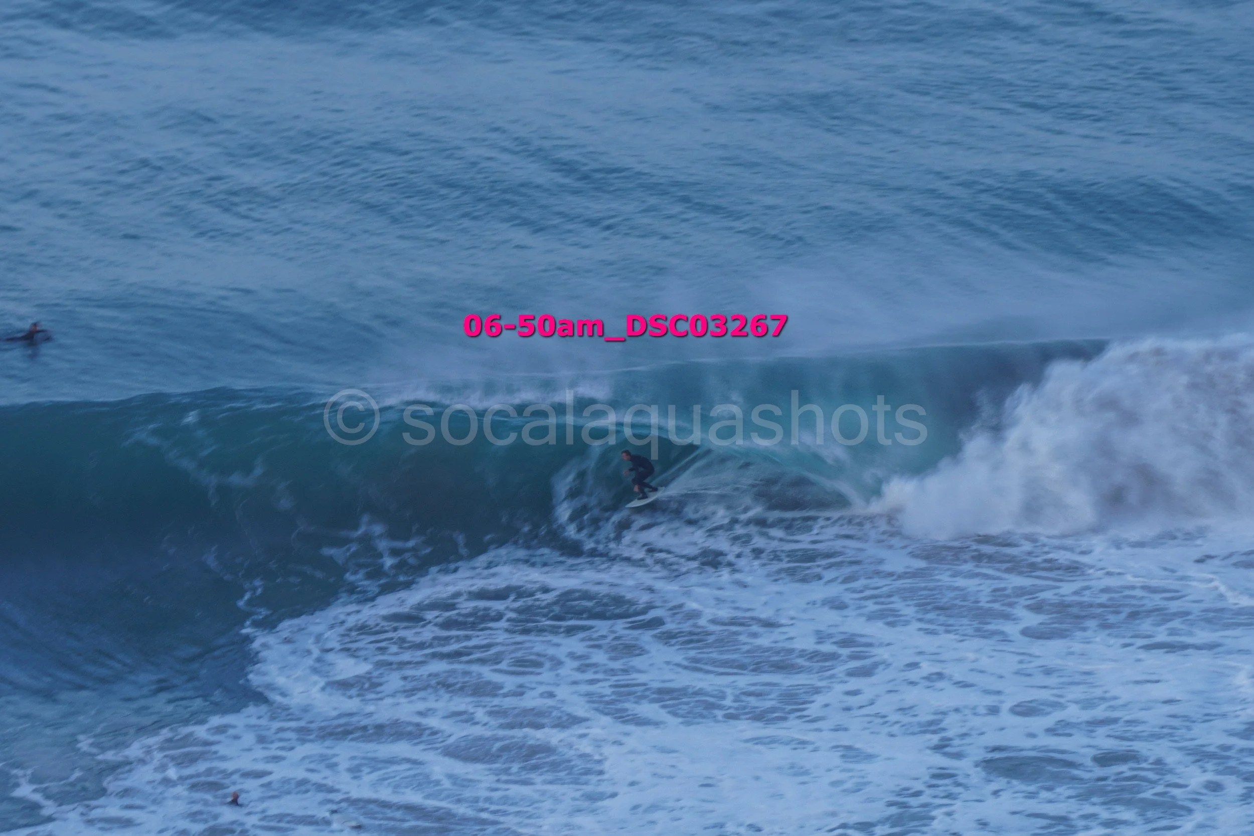 A person surfing on a wave in the ocean, with another surfer in the background, during early morning.