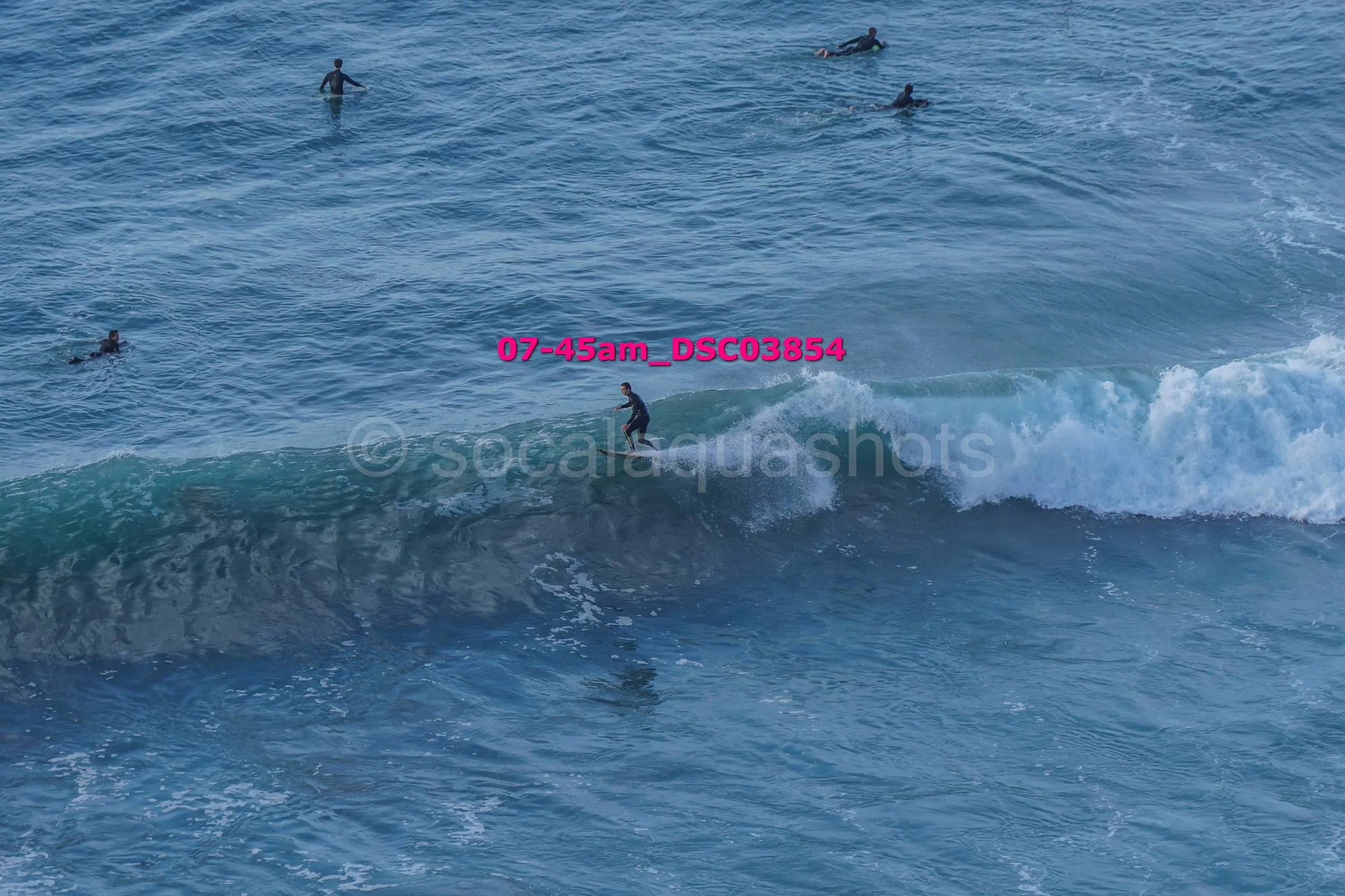 A person surfing on a wave with several other surfers in the water nearby.