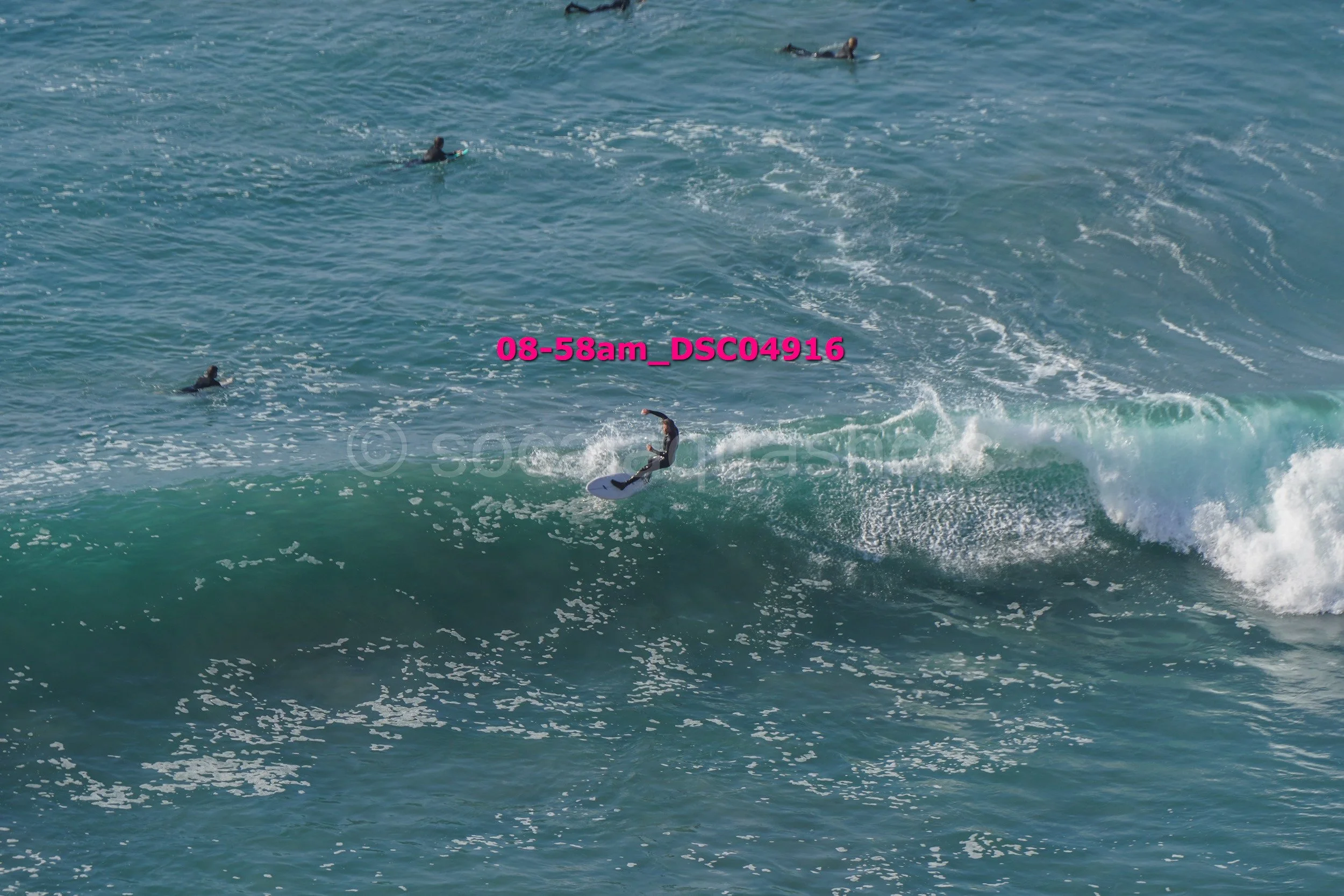 Surfer riding a wave with several surfers in the background on the ocean.