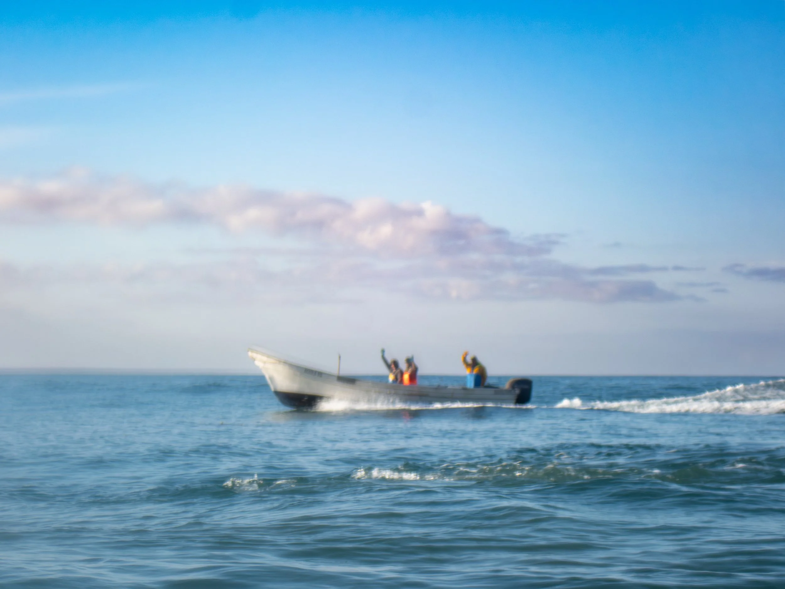 A small motorboat with four people on board traveling across the ocean, under a sky with scattered clouds.