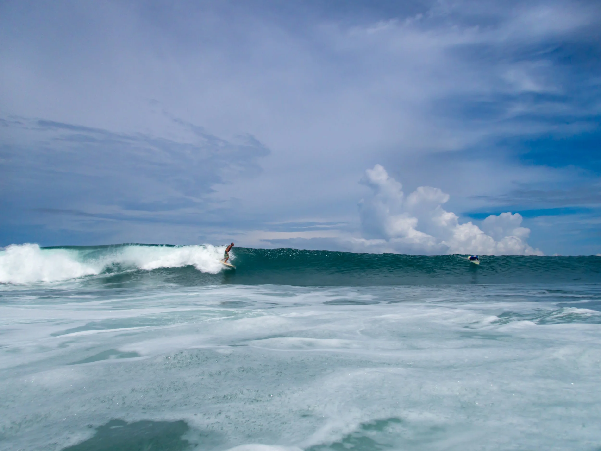 Surfer riding a wave in the ocean under a cloudy sky.