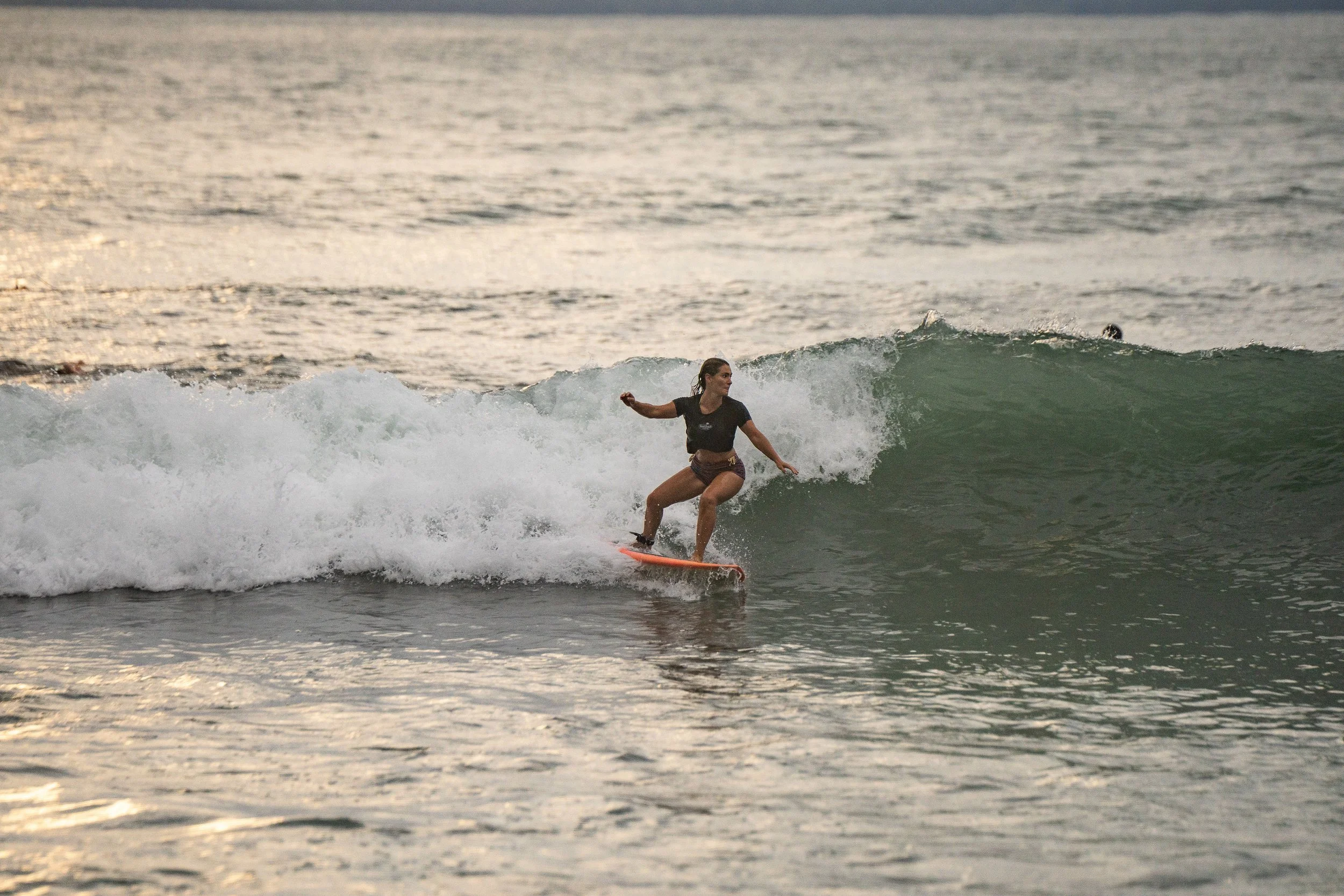A woman surfing on a small wave at the beach during sunset.