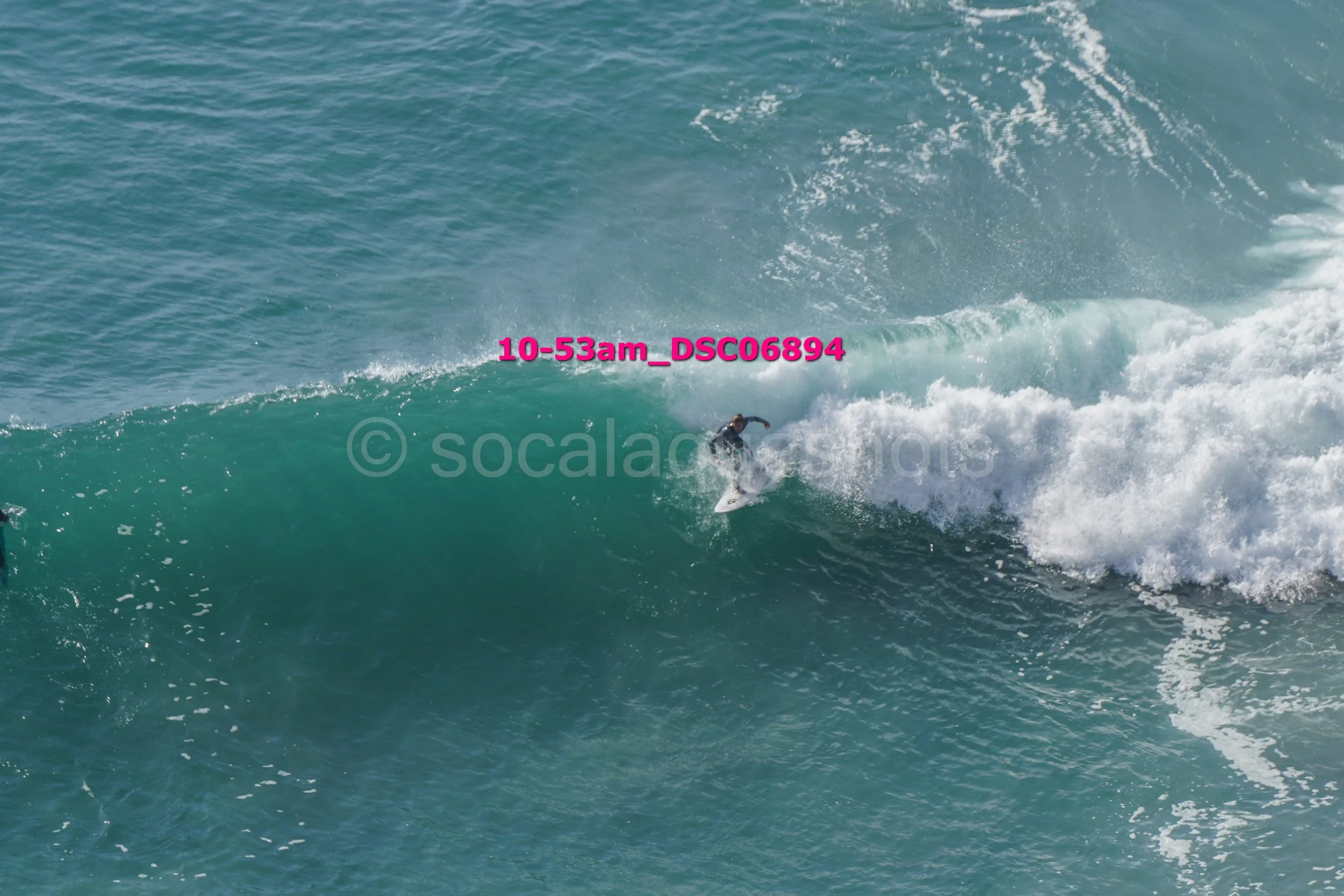Person surfing on a large blue-green wave in the ocean.