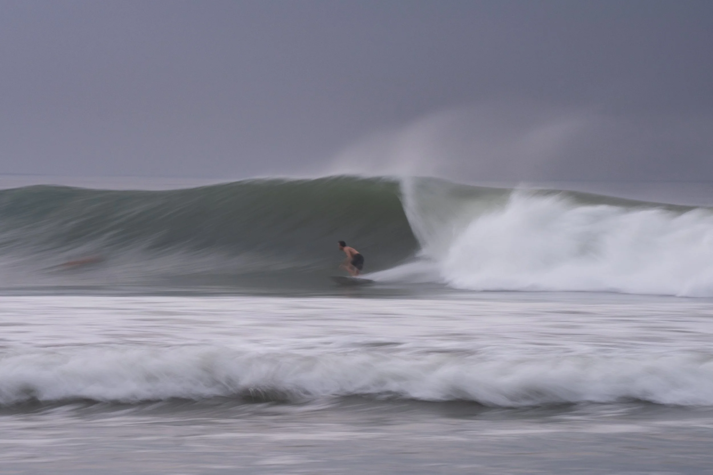 A person surfing on a wave in the ocean under a cloudy sky.