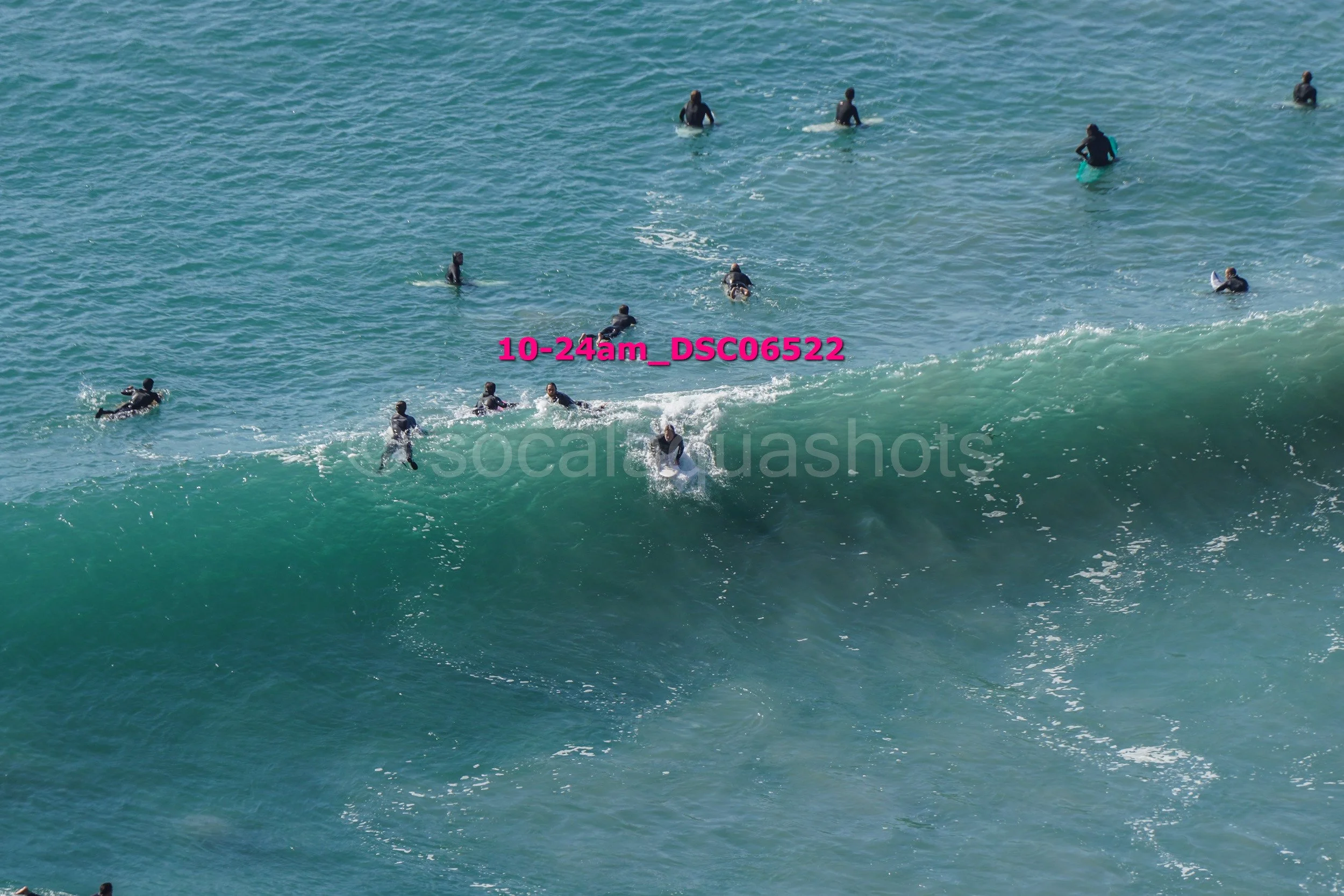 Surfers riding a wave at the beach, with some surfers paddling in the water.