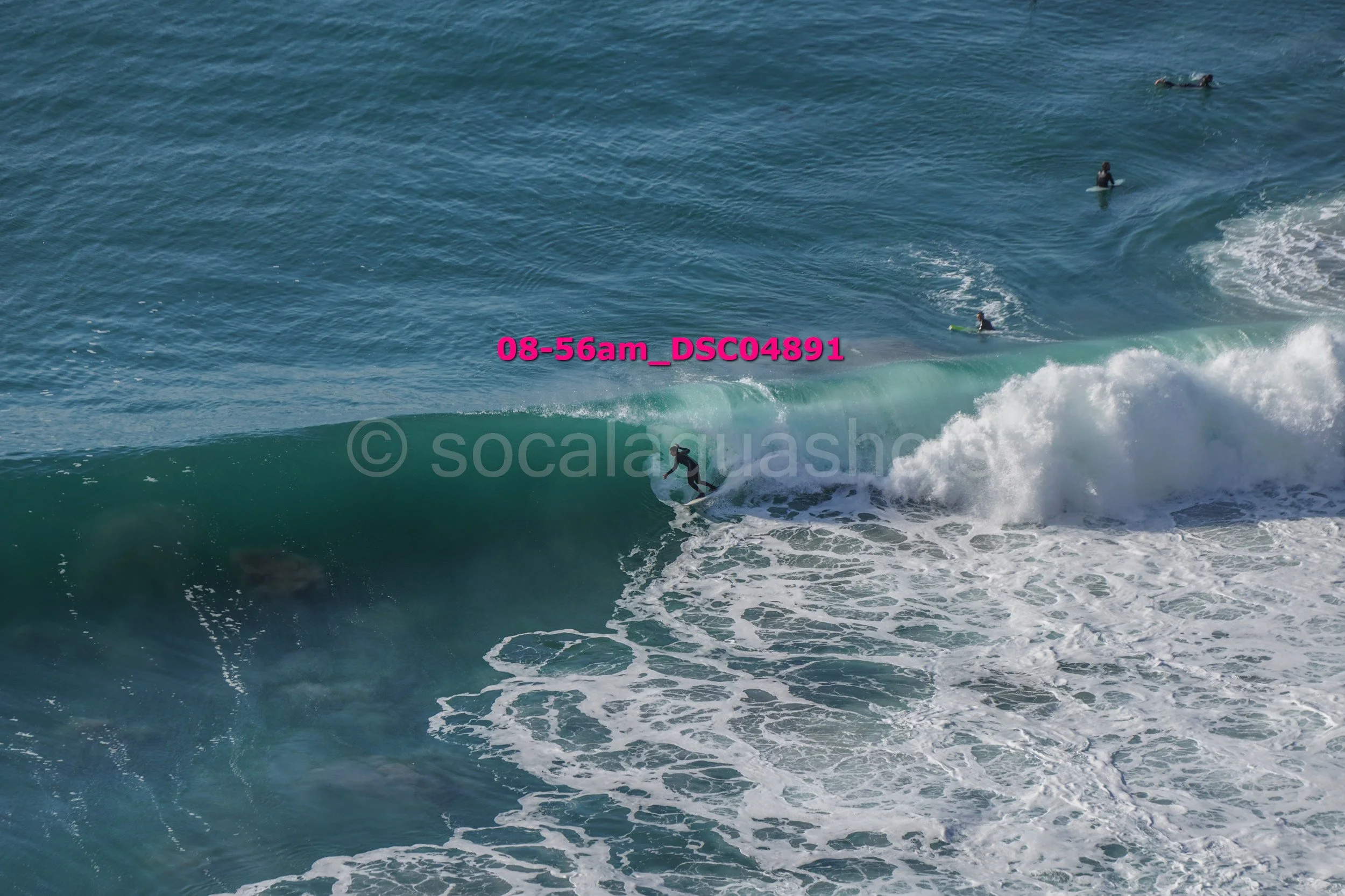 Surfer riding a wave in the ocean with several other surfers in the background.