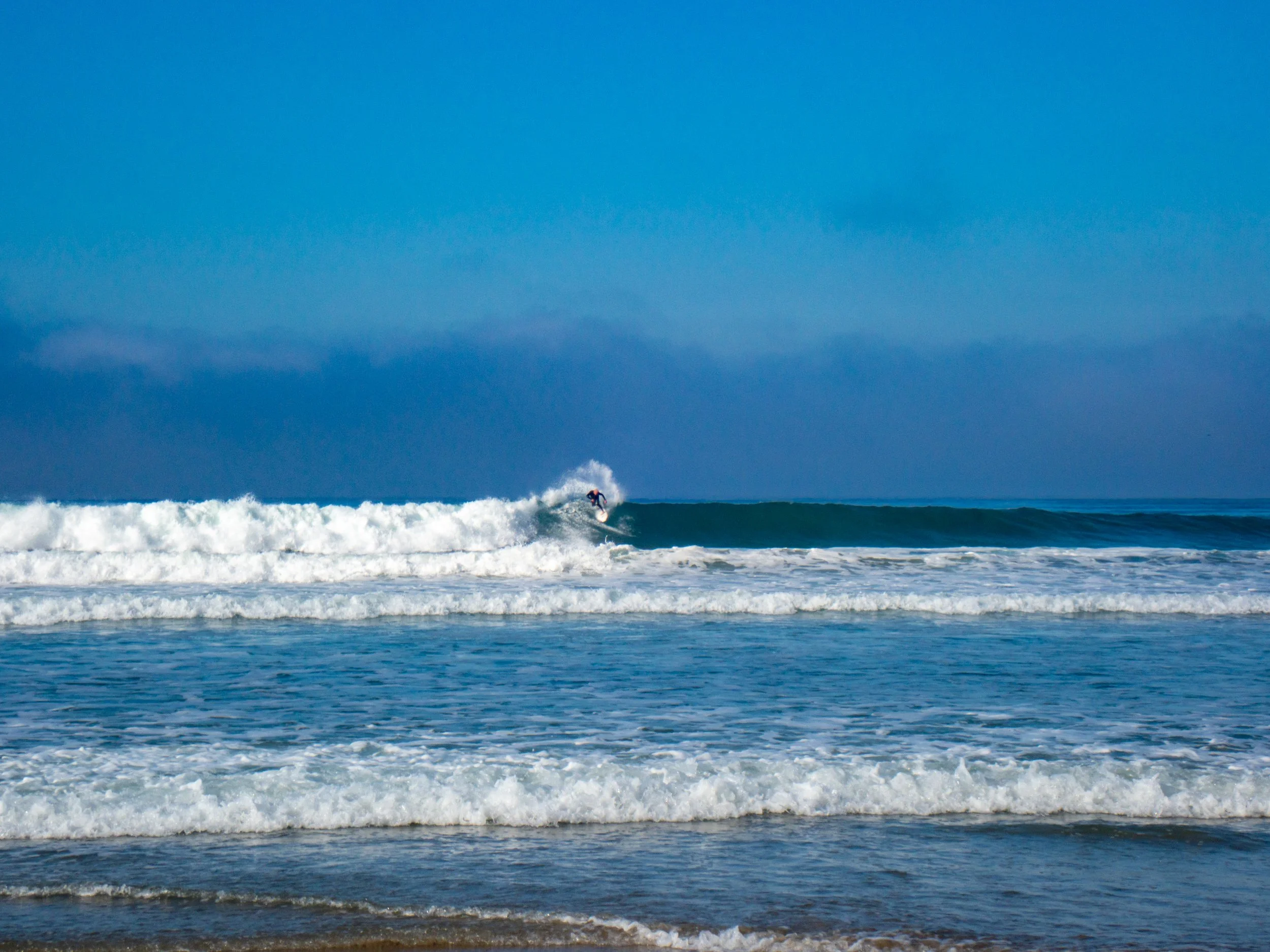 A person surfing on a wave in the ocean with a clear blue sky above.