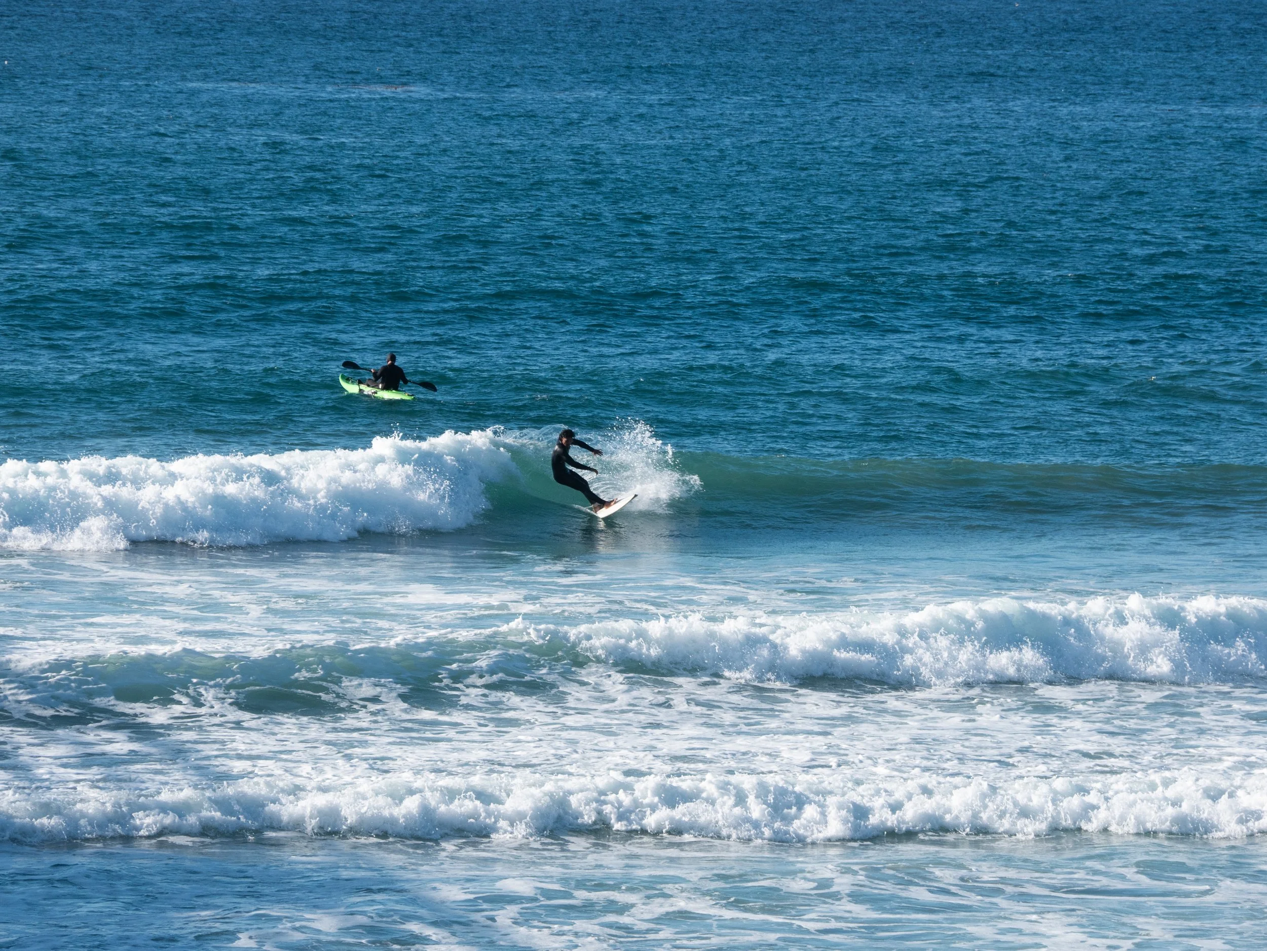 Person surfing on a wave with a kayak and kayaker in the background in the ocean.