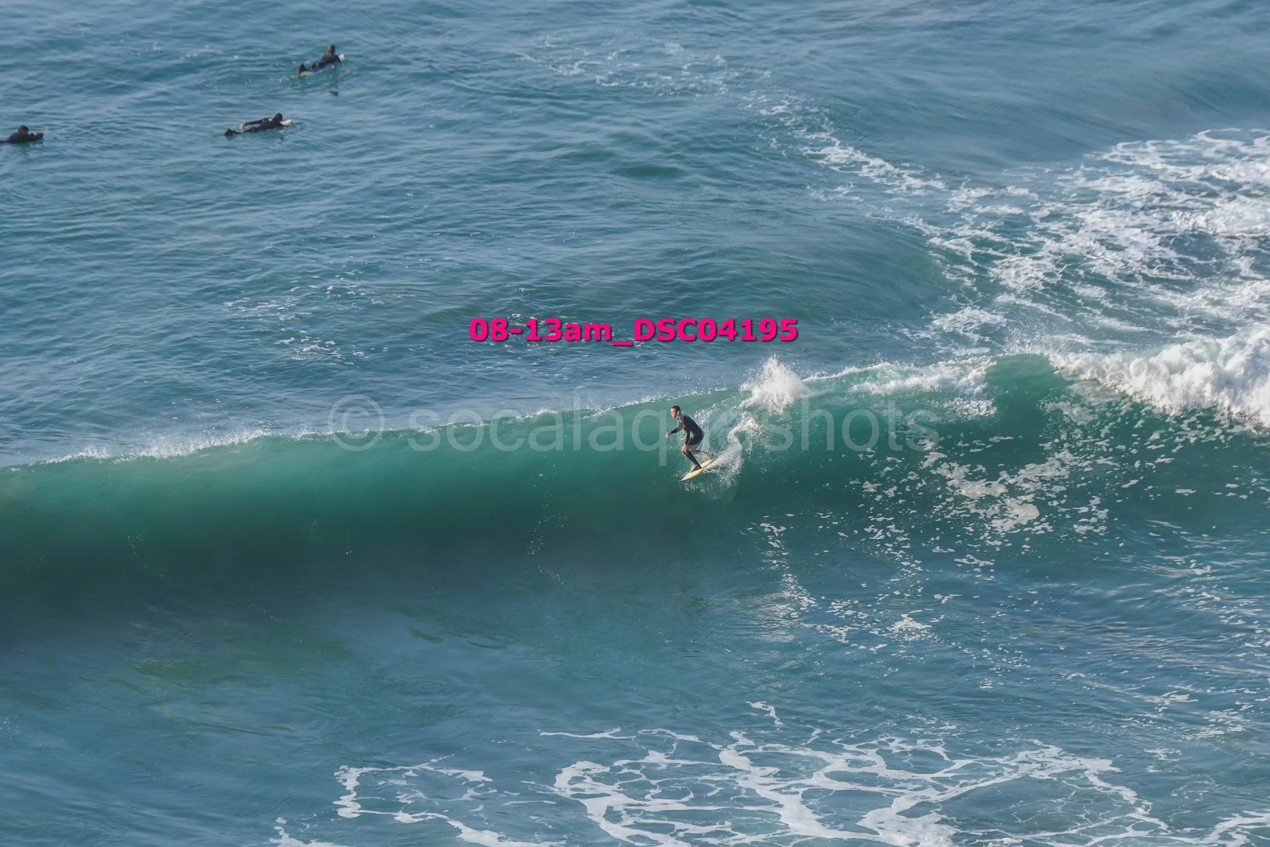 A surfer riding a wave in the ocean with several other surfers floating on their boards in the water nearby.