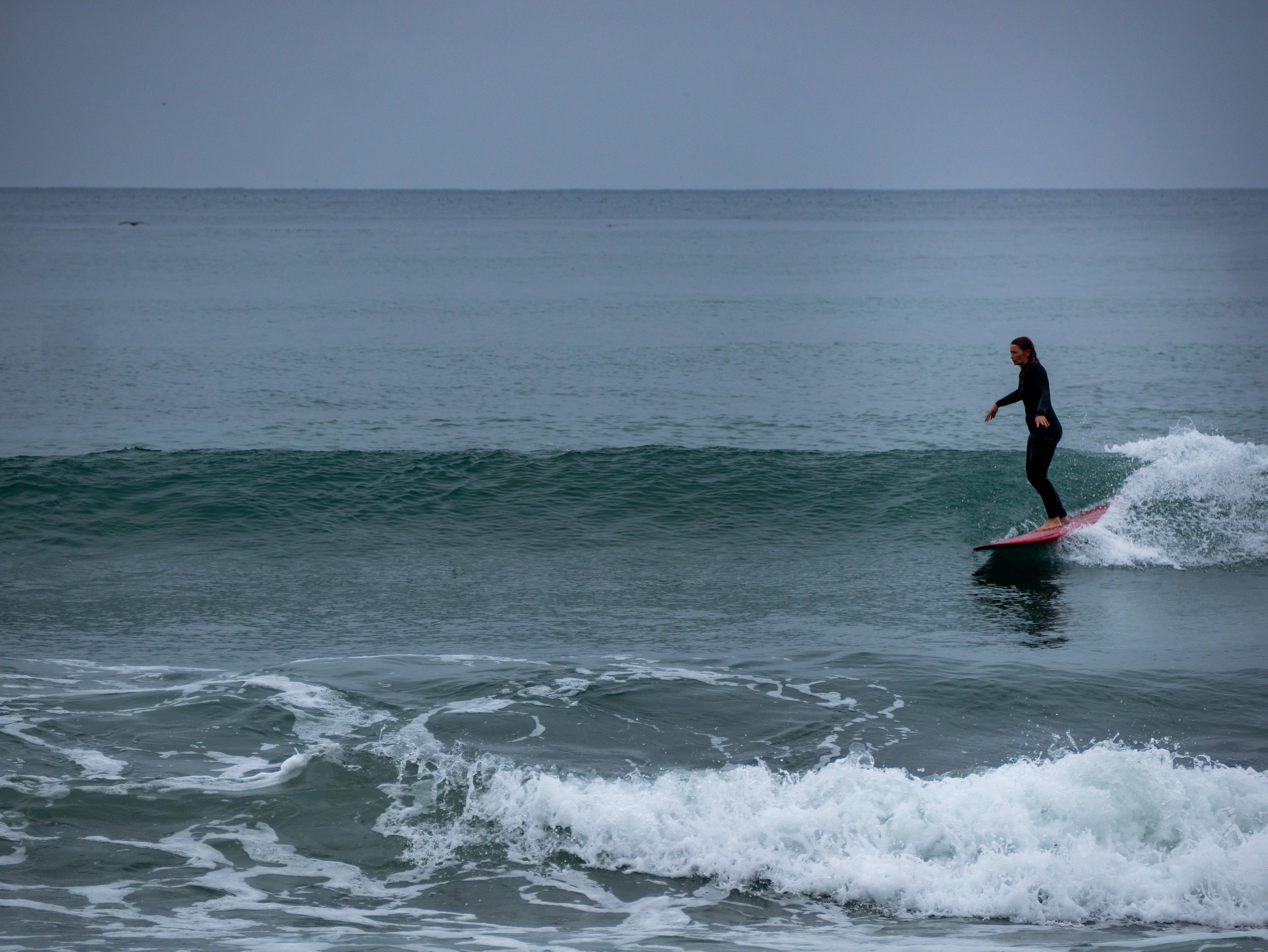 A person surfing on a small wave in the ocean during overcast weather.