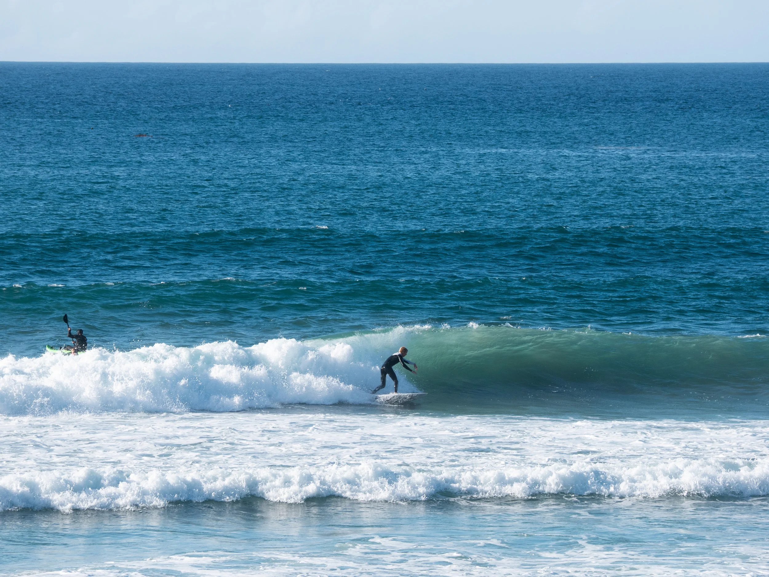 Two surfers riding waves in the ocean with blue sky above.