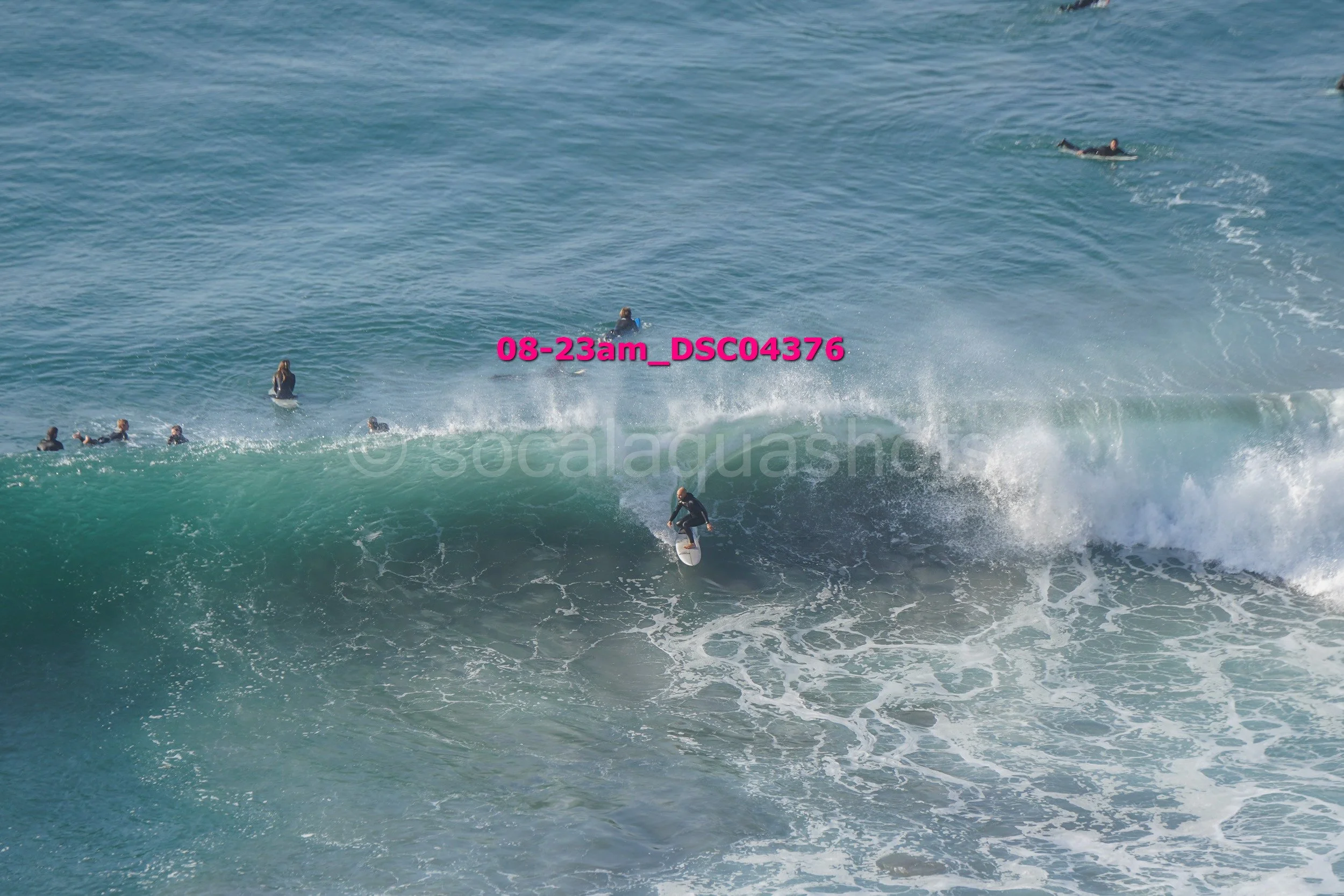 Surfer riding a wave with multiple people in the water nearby.
