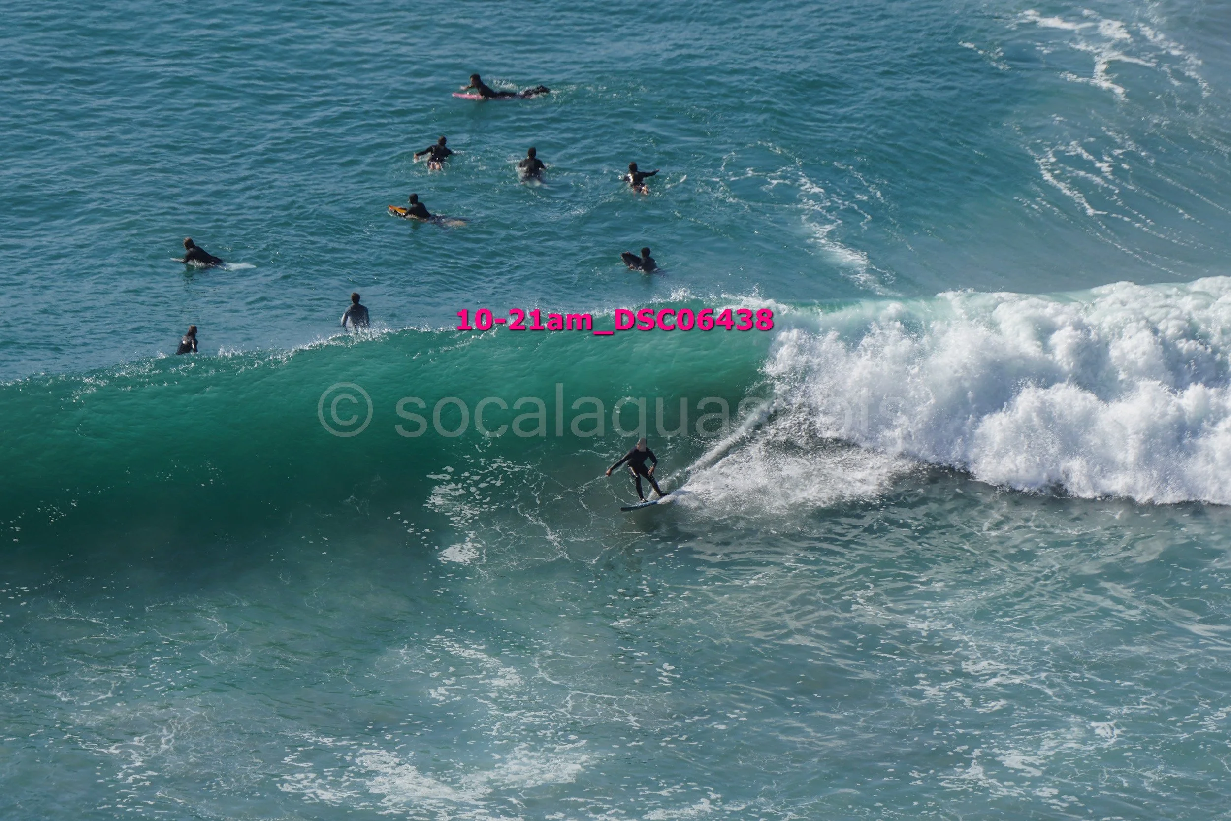 Surfer riding a large wave with multiple surfers in the water in the background.
