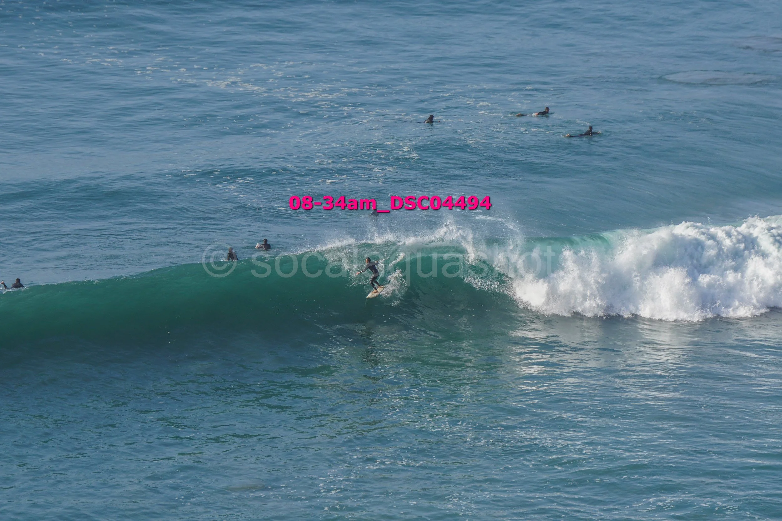 A person surfing a wave with several other surfers in the water.