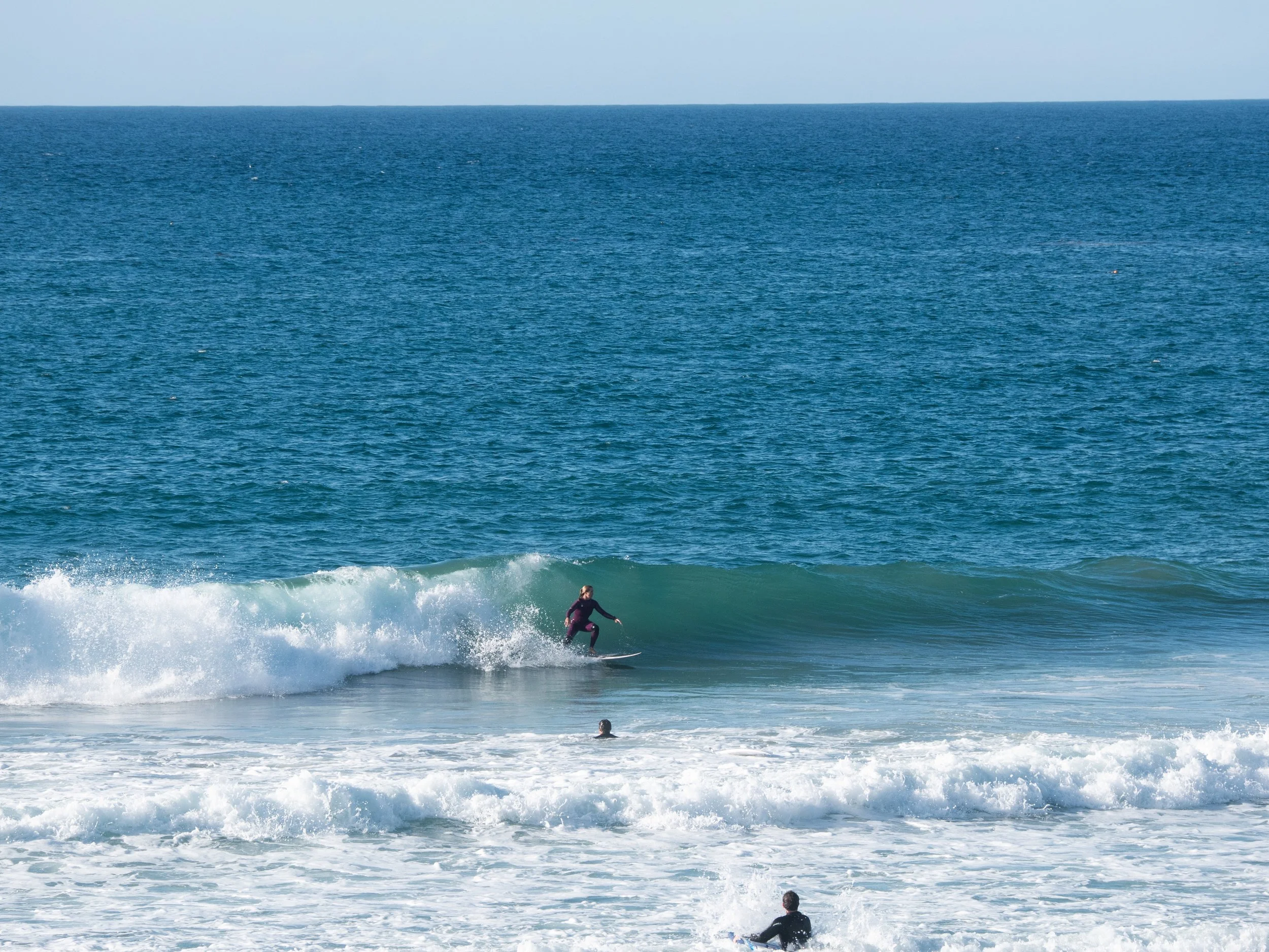 A person surfing on a wave in the ocean with a clear blue sky.