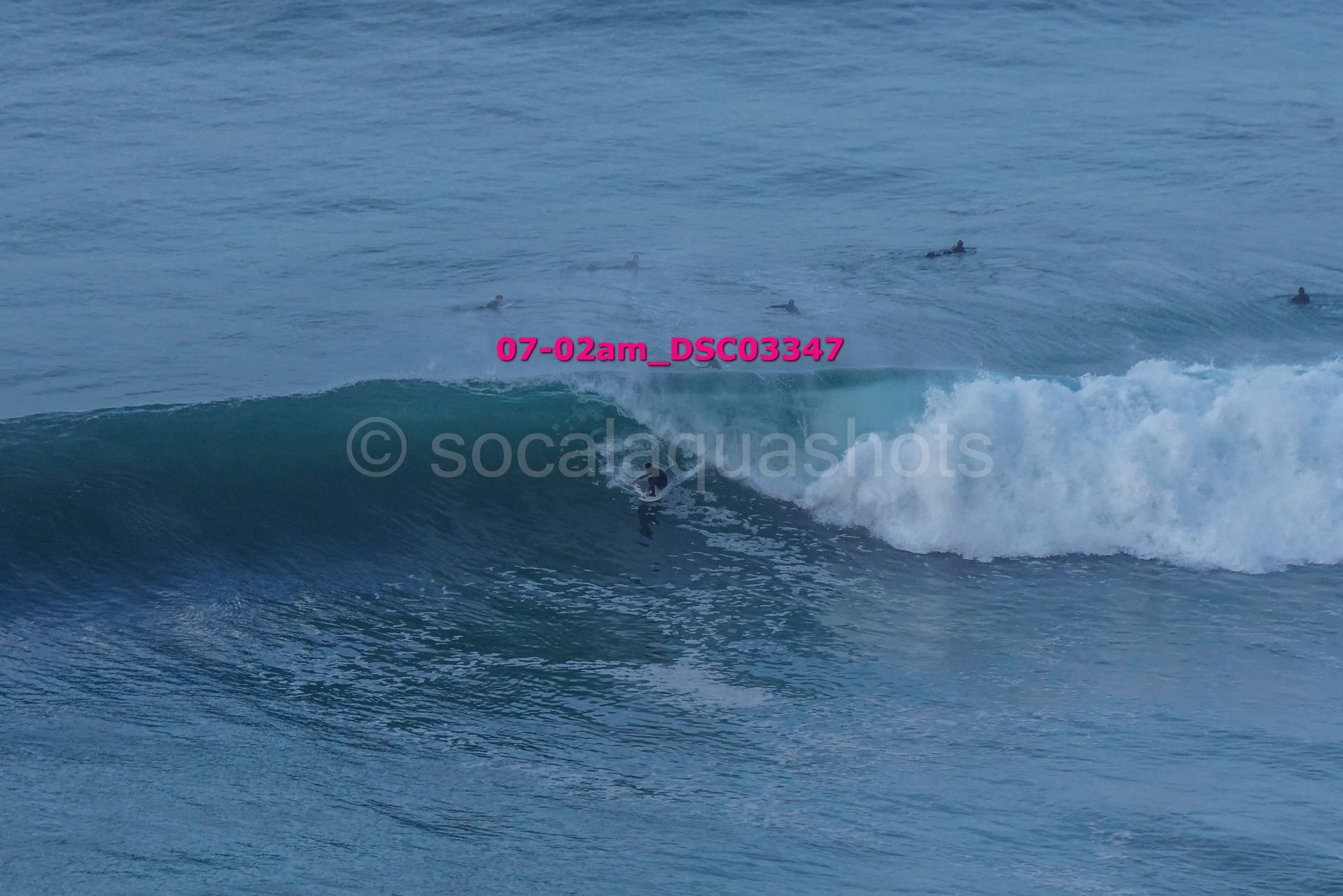 A person surfing a wave in the ocean with several surfers visible in the background.