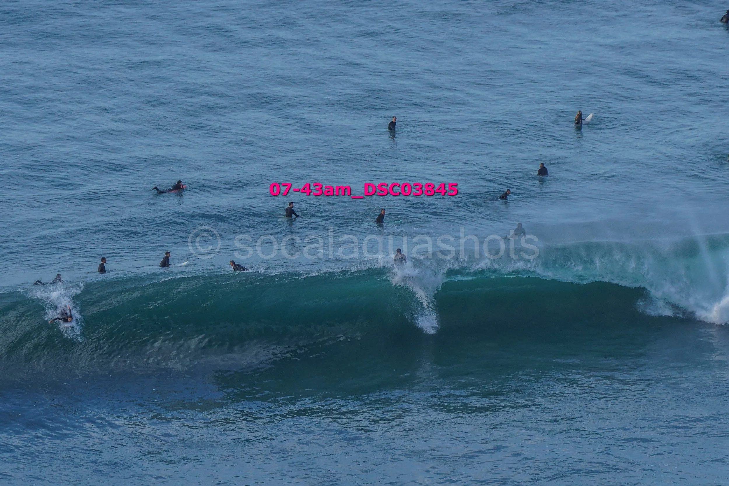 Surfers waiting in the water near a breaking wave at the beach early in the morning.