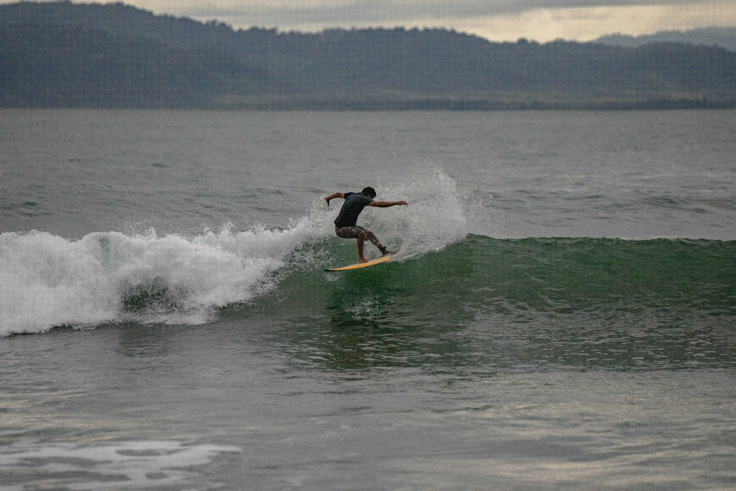 A person surfing on a wave in the ocean during overcast weather.