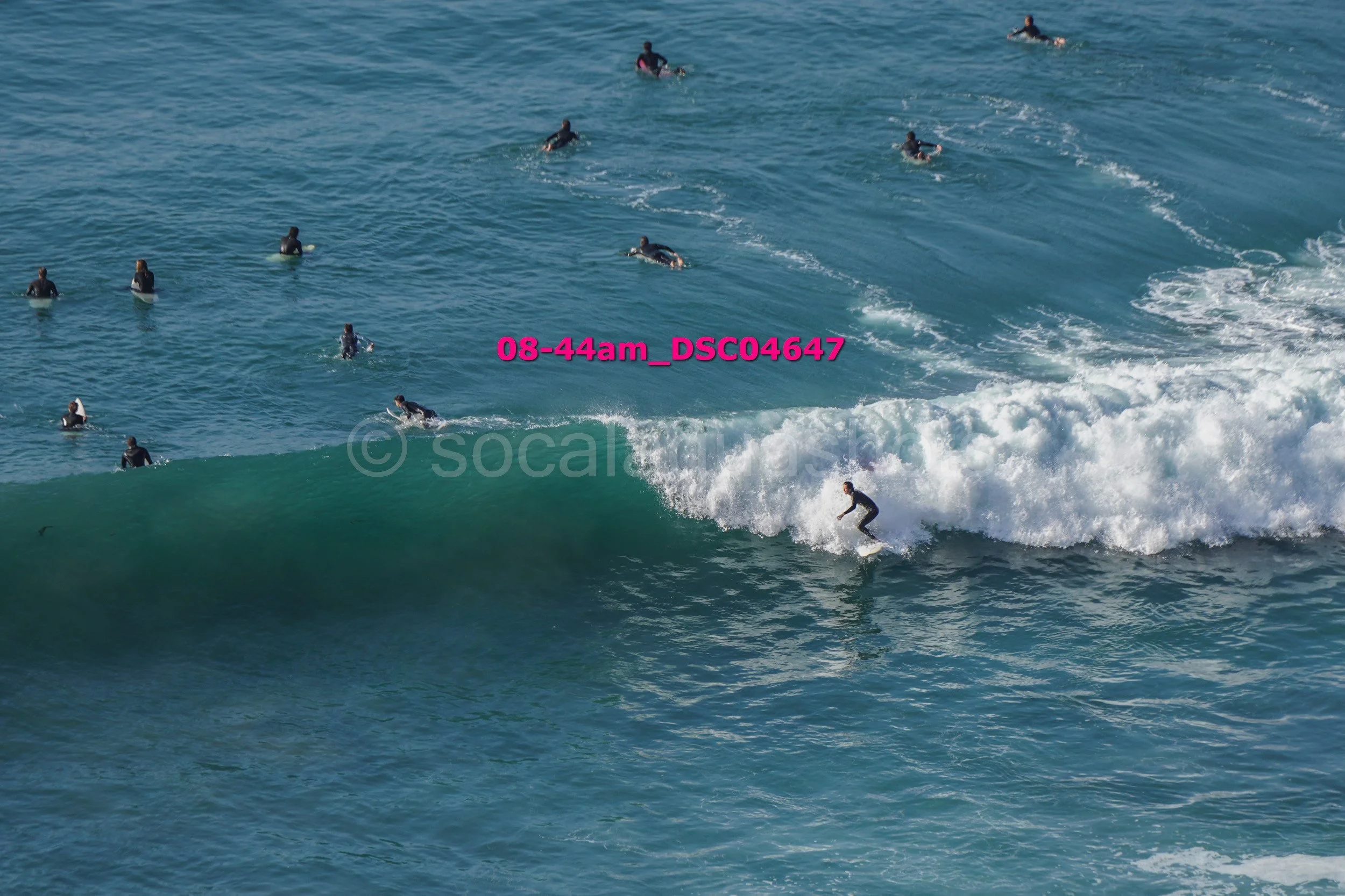 A person surfing on a wave with multiple other surfers in the water behind them.