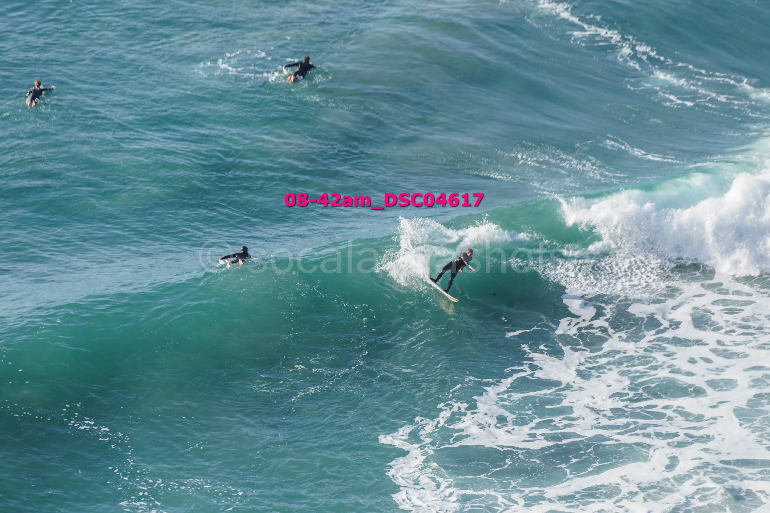 Surfer riding a wave with three other surfers in the water nearby.