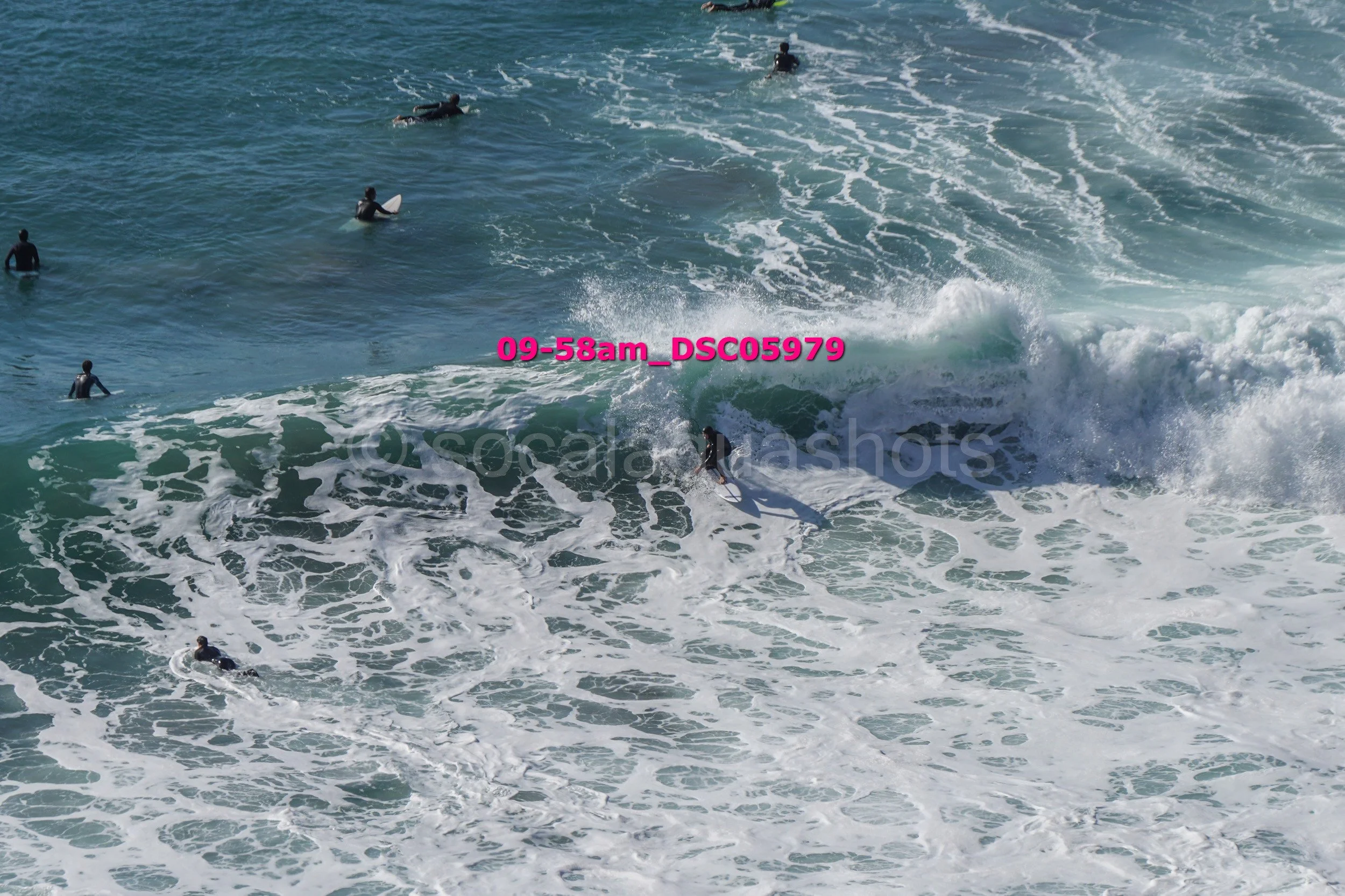 Surfers in the ocean riding and waiting for waves with foamy water and surfboards.