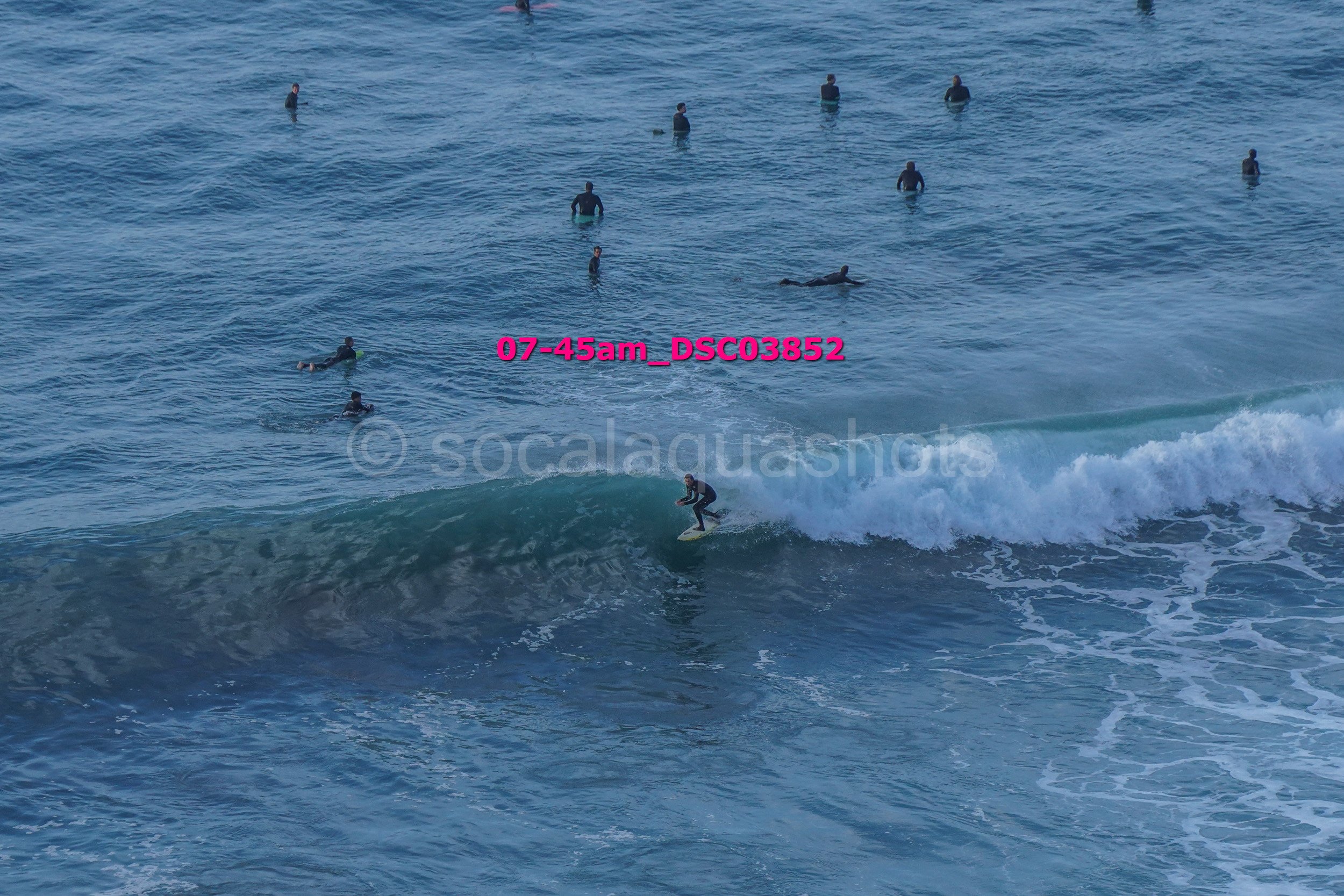 A person surfing on a wave in the ocean with several others swimming and floating in the water nearby.