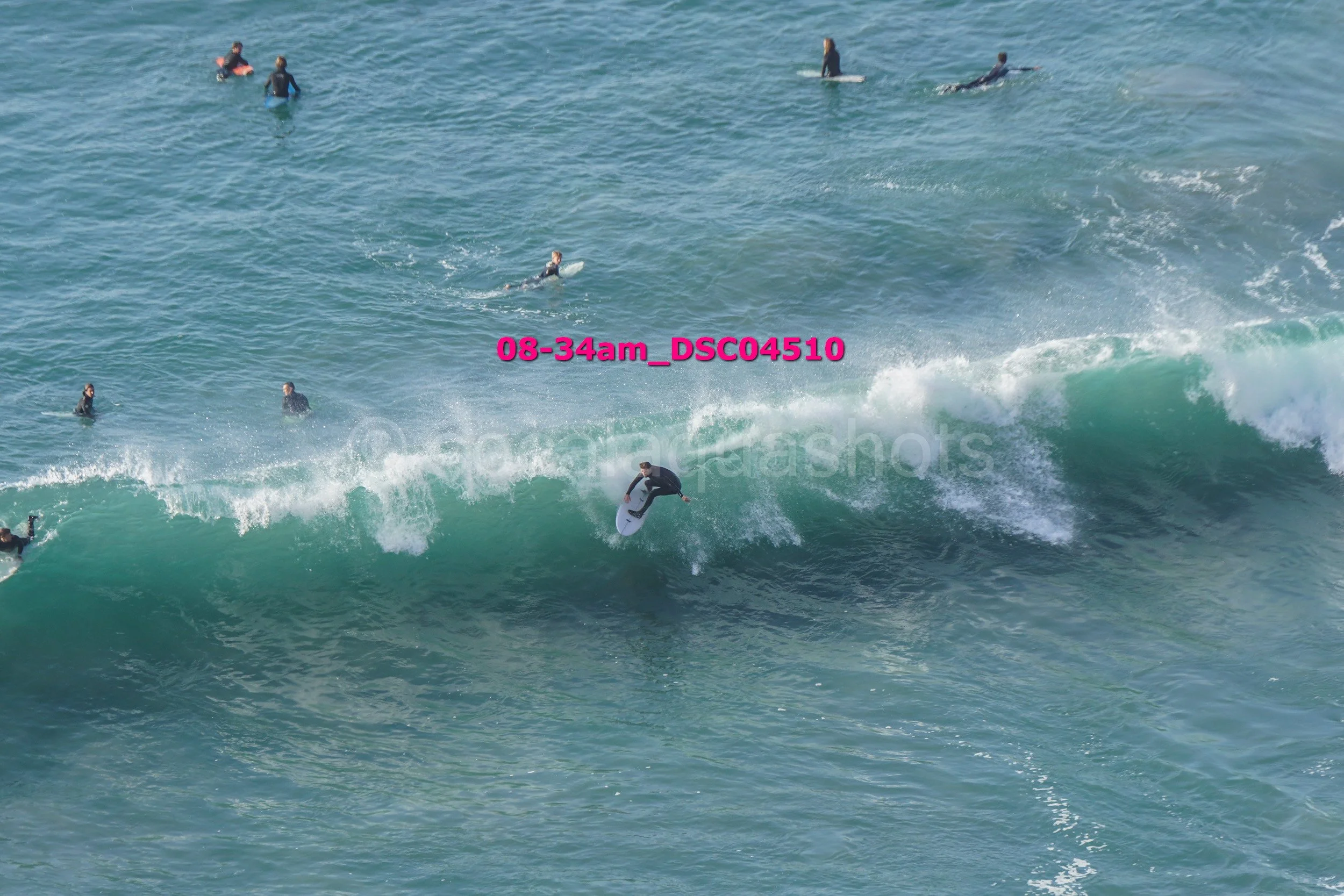Surfer riding a large wave with several people in the water in the background.