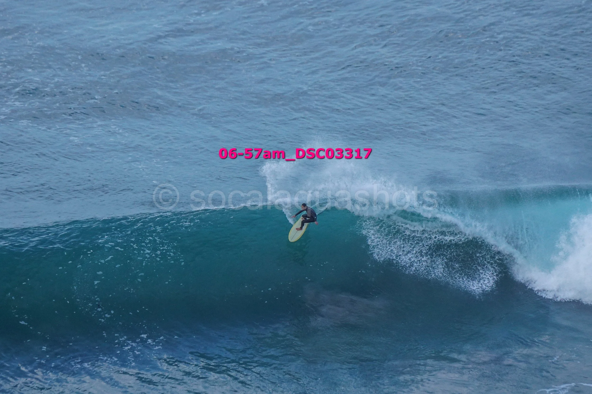 A person surfing on a large blue ocean wave with a clear sky in the background.
