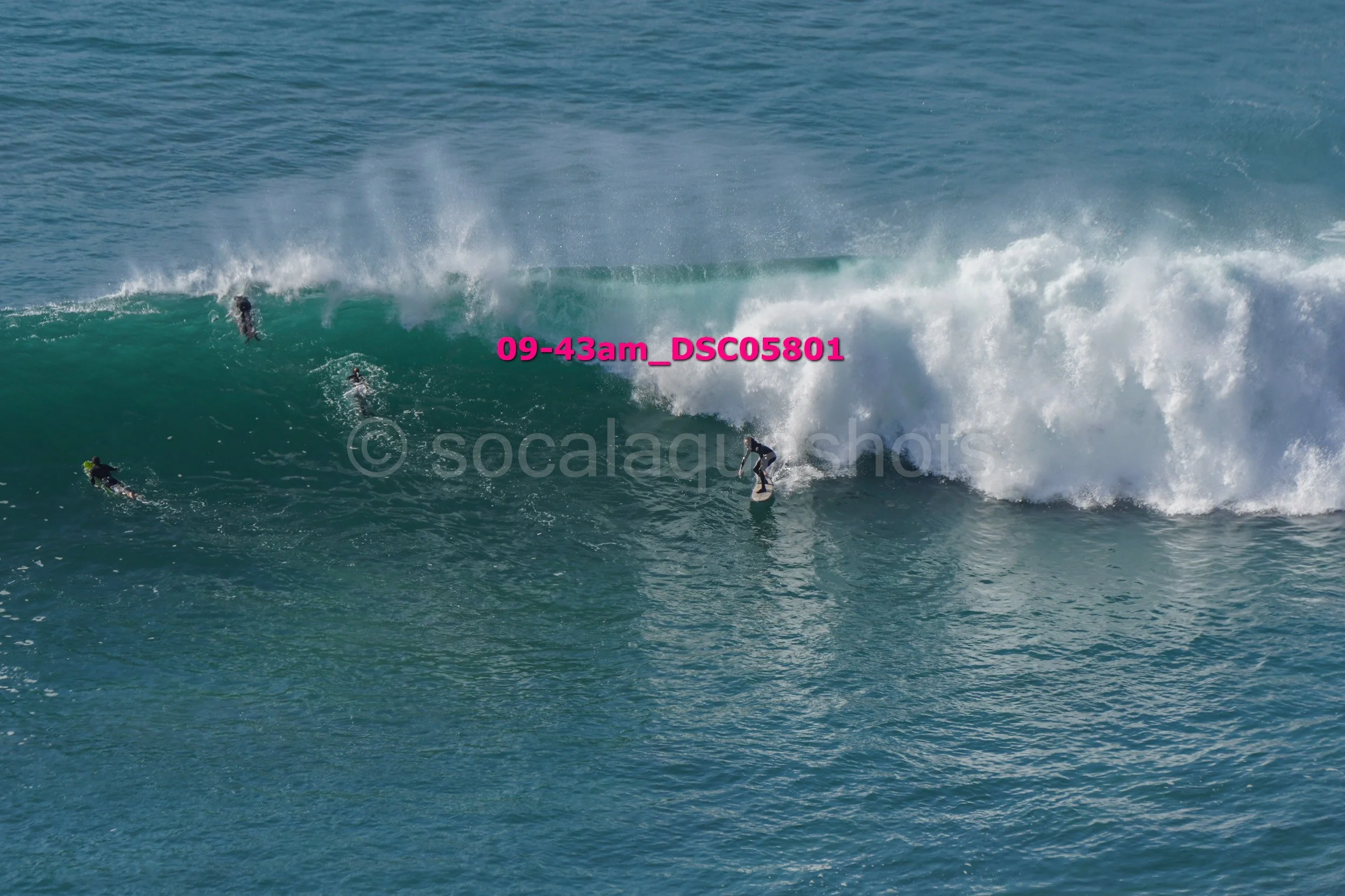 Surfers riding large ocean waves, with some surfers paddling and others executing maneuvers on their surfboards.