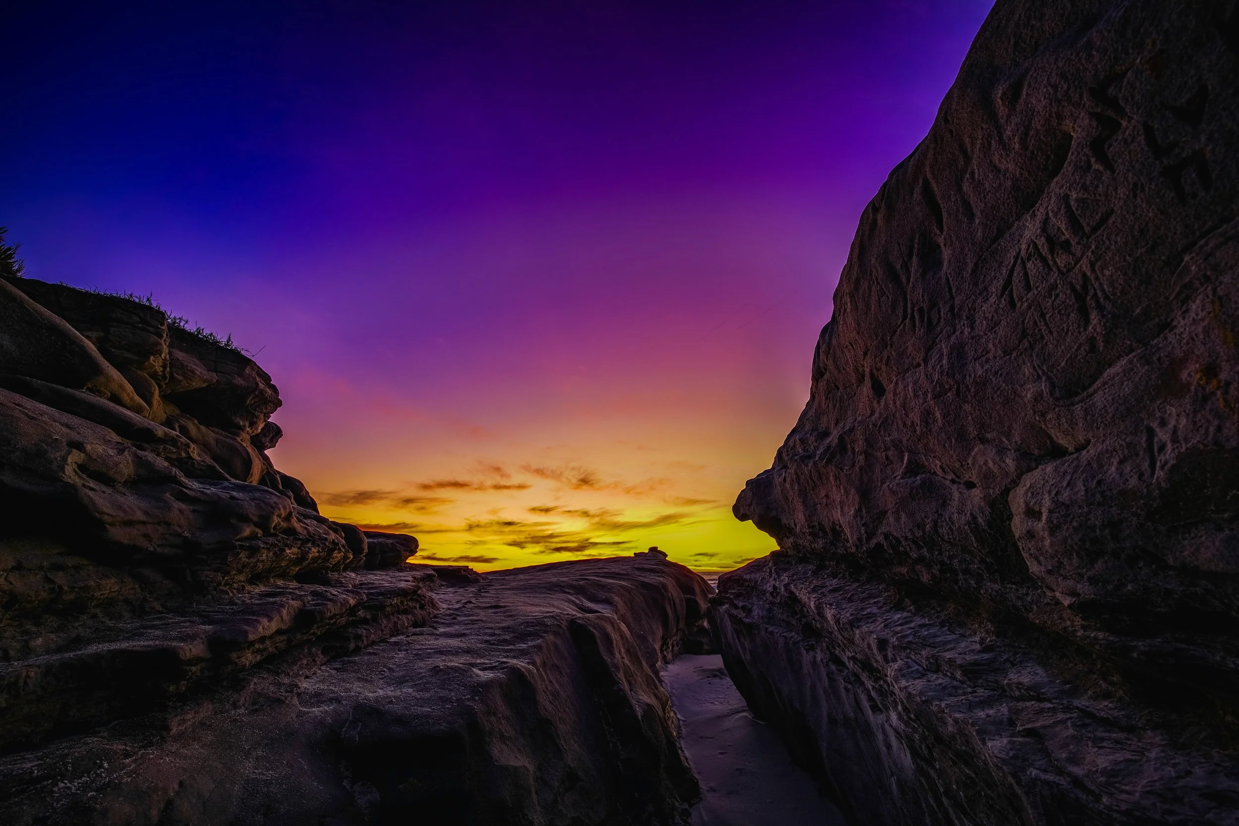 Sunset over rocky coastal landscape with colorful purple, yellow, and orange sky.
