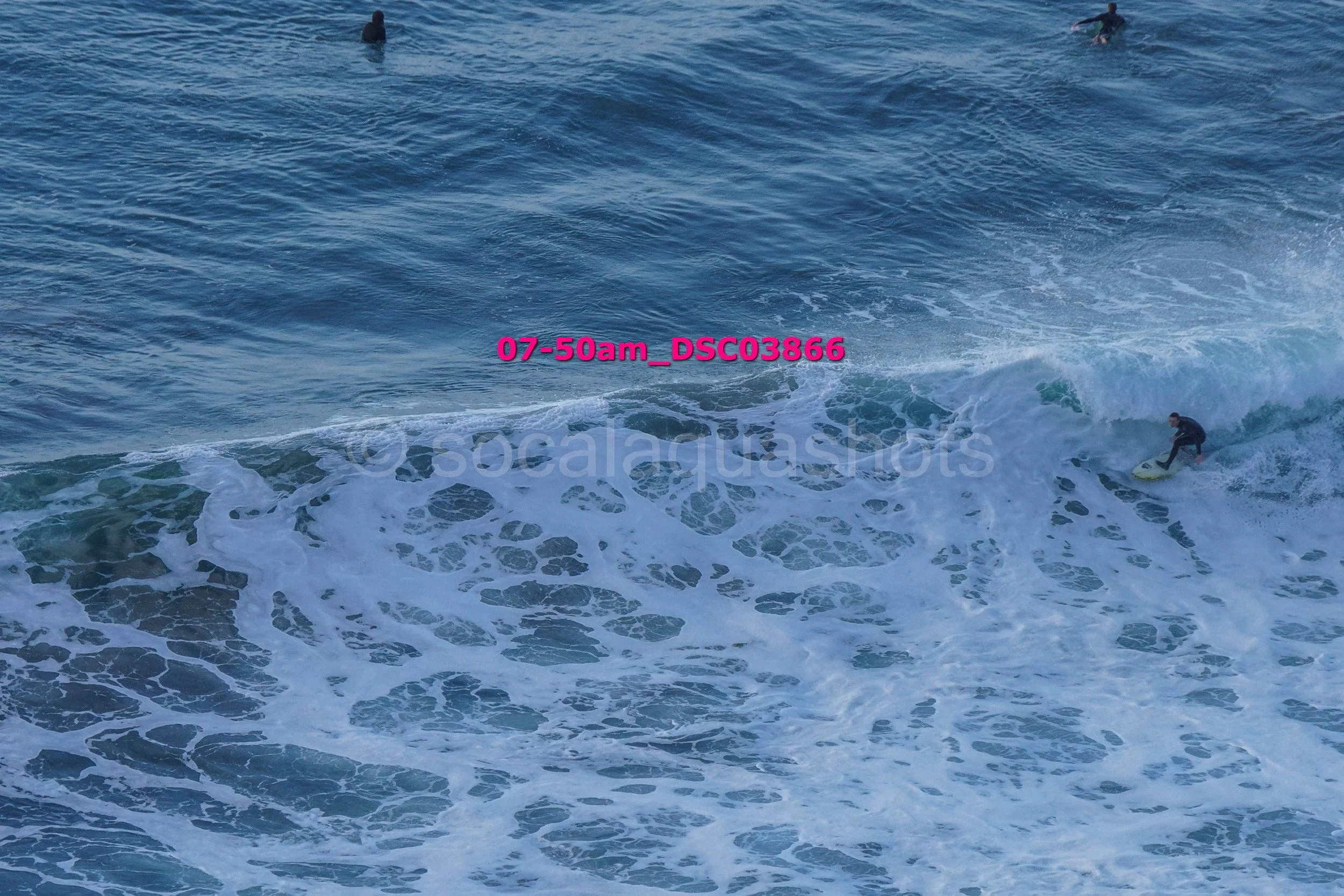 A person surfing on a wave in the ocean with a few other surfers visible in the background.