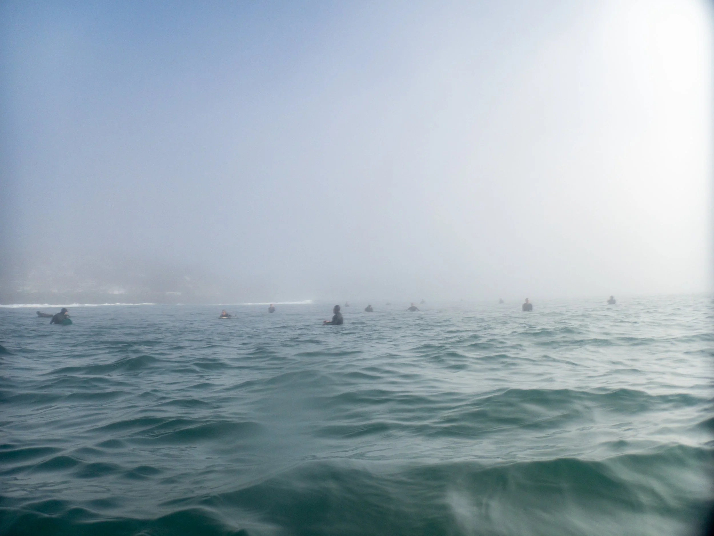 A group of people surfing in the ocean on a foggy day.