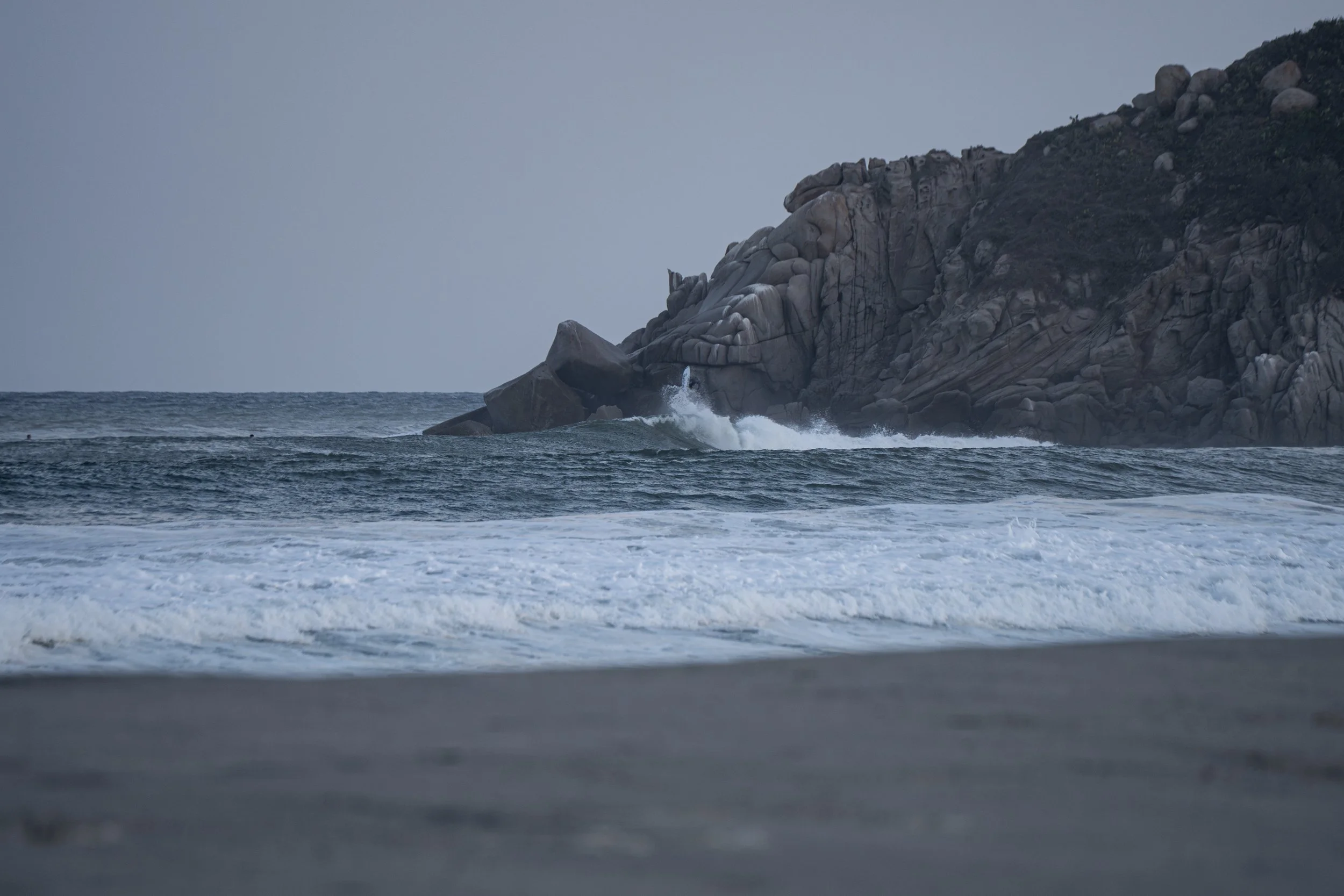 Ocean waves crashing against a rocky cliff on a cloudy day.