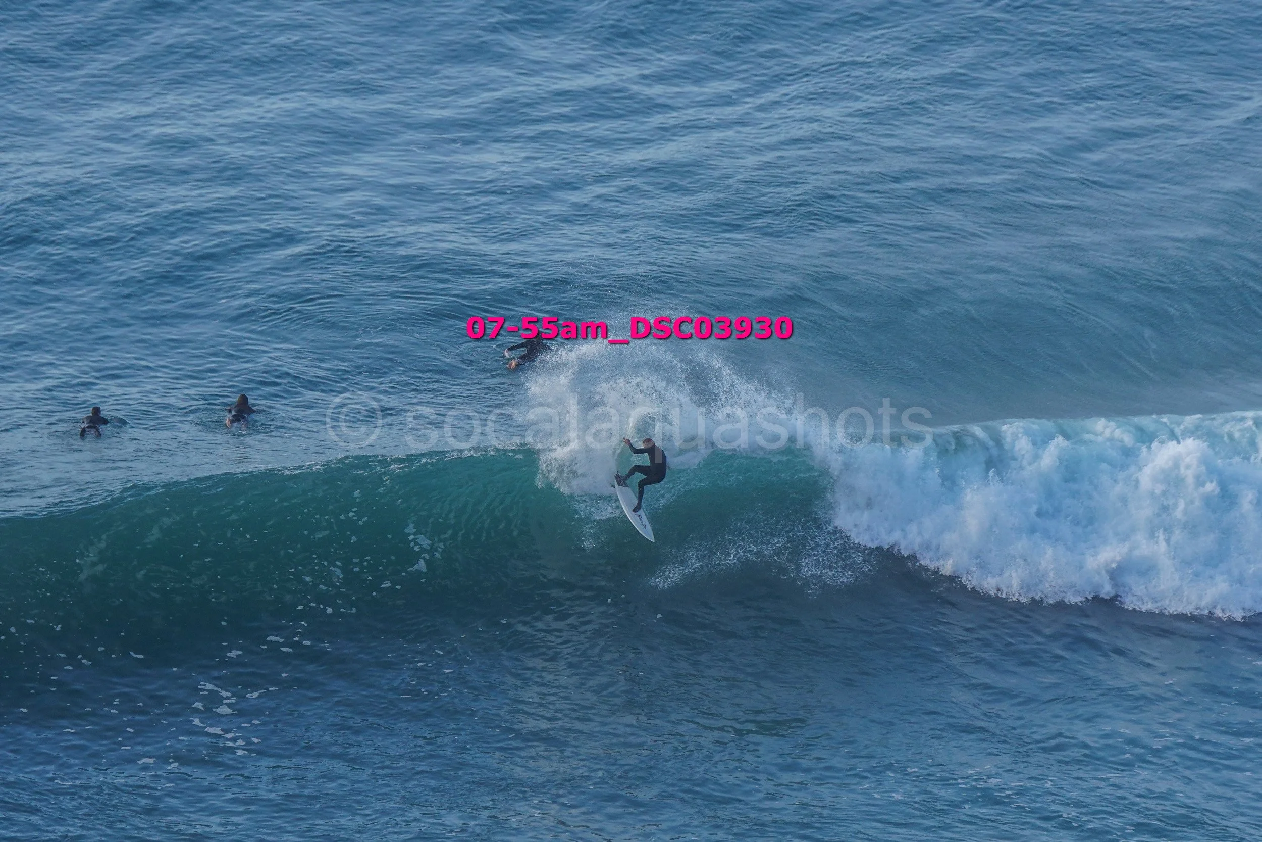 A person surfing on a wave with three other surfers in the water nearby.