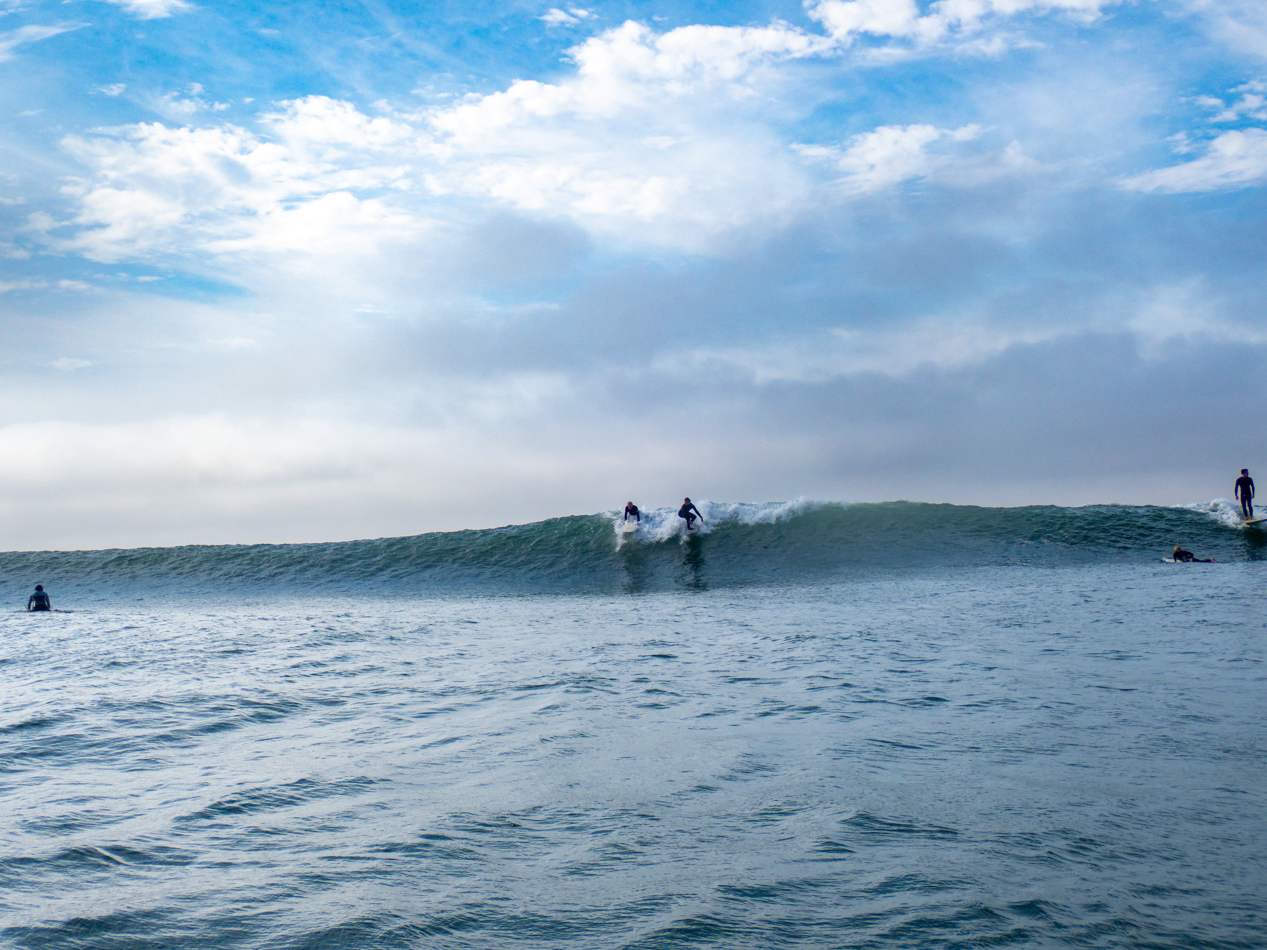 People surfing on ocean waves on a partly cloudy day.