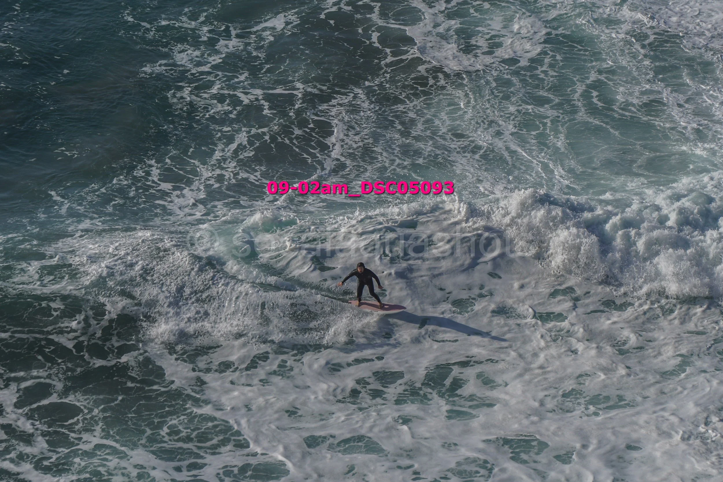A person surfing on the ocean waves in the distance, with foamy water surrounding them.